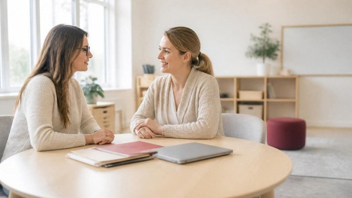 Teacher and parent talking at a table in a bright school meeting room