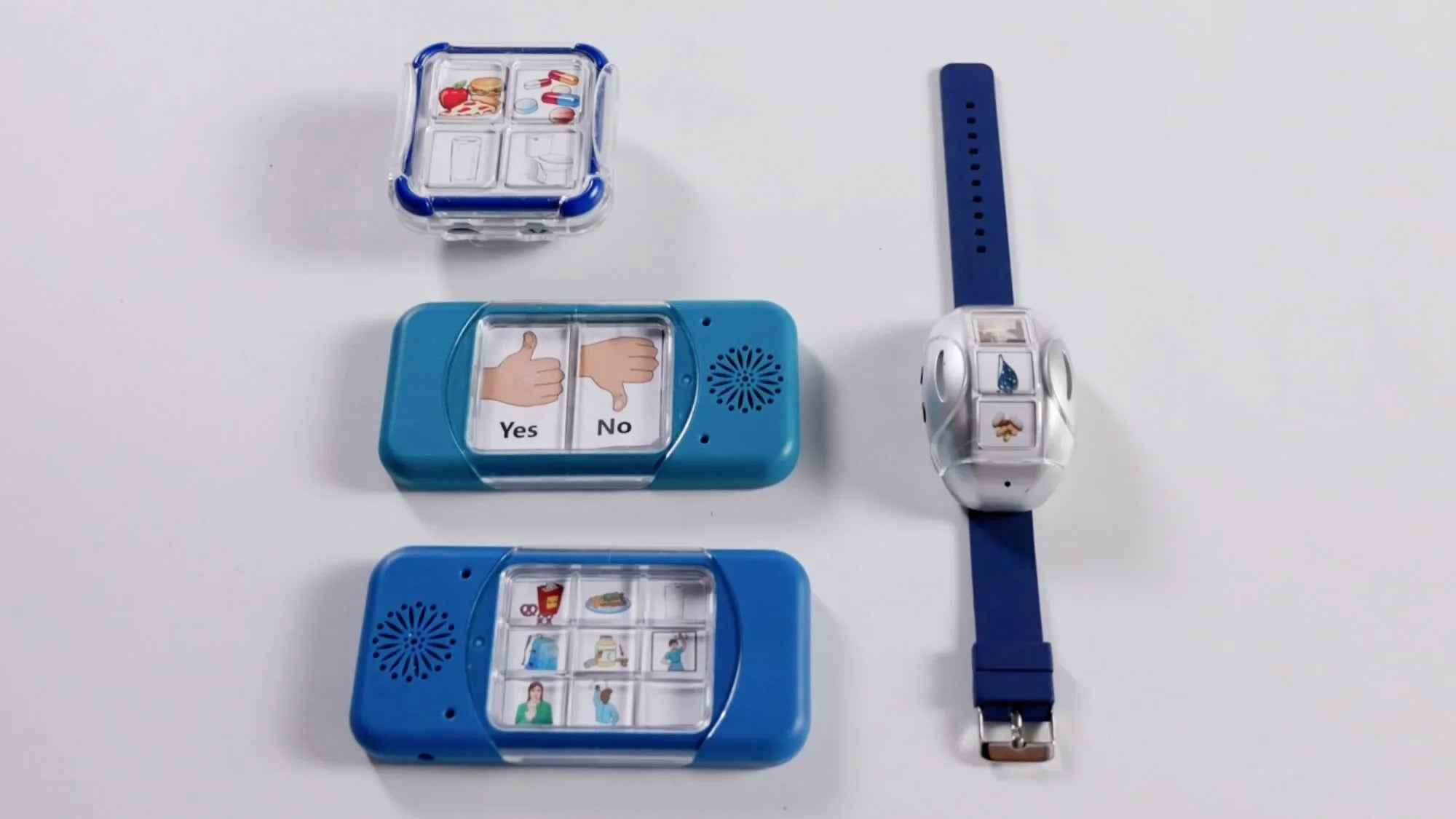 Four assistive communication devices are displayed on a white surface: a small square device, two rectangular blue devices with picture buttons, and a blue wristband device with communication symbols.
