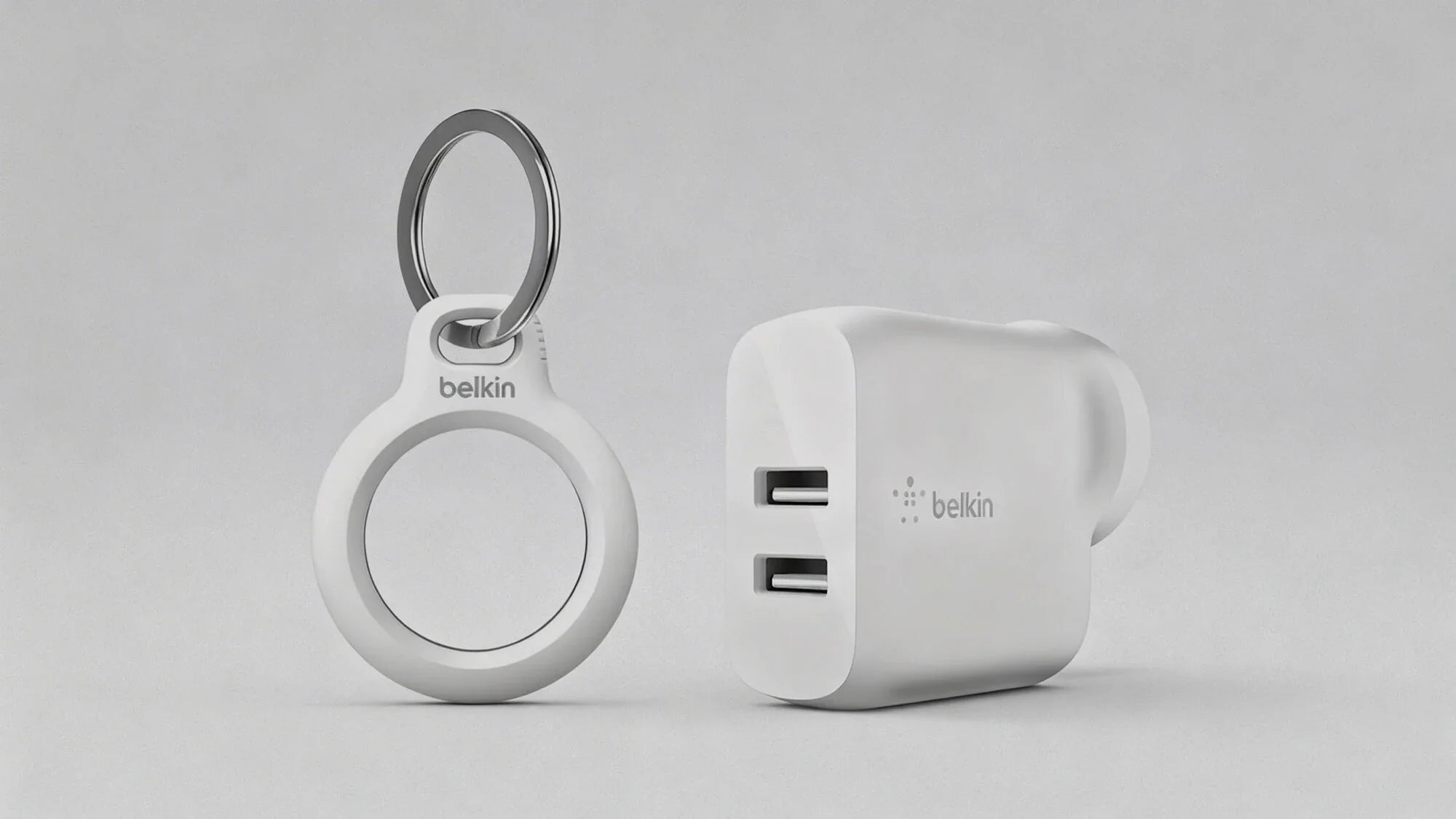A white Belkin keychain holder with a circular opening sits next to a white Belkin USB wall charger featuring two USB ports, both on a light gray background.