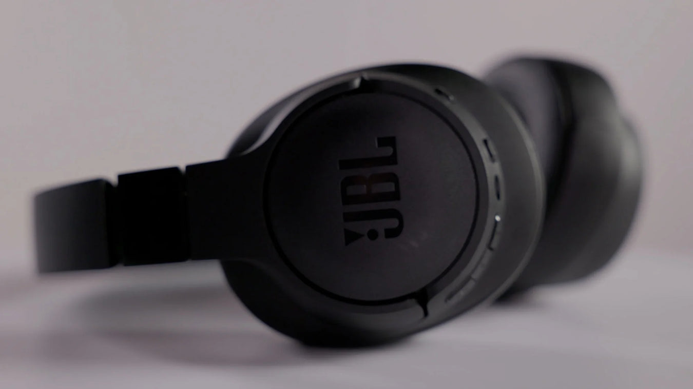 Close-up view of black JBL over-ear headphones with the JBL logo visible on the ear cup, set against a plain light background.