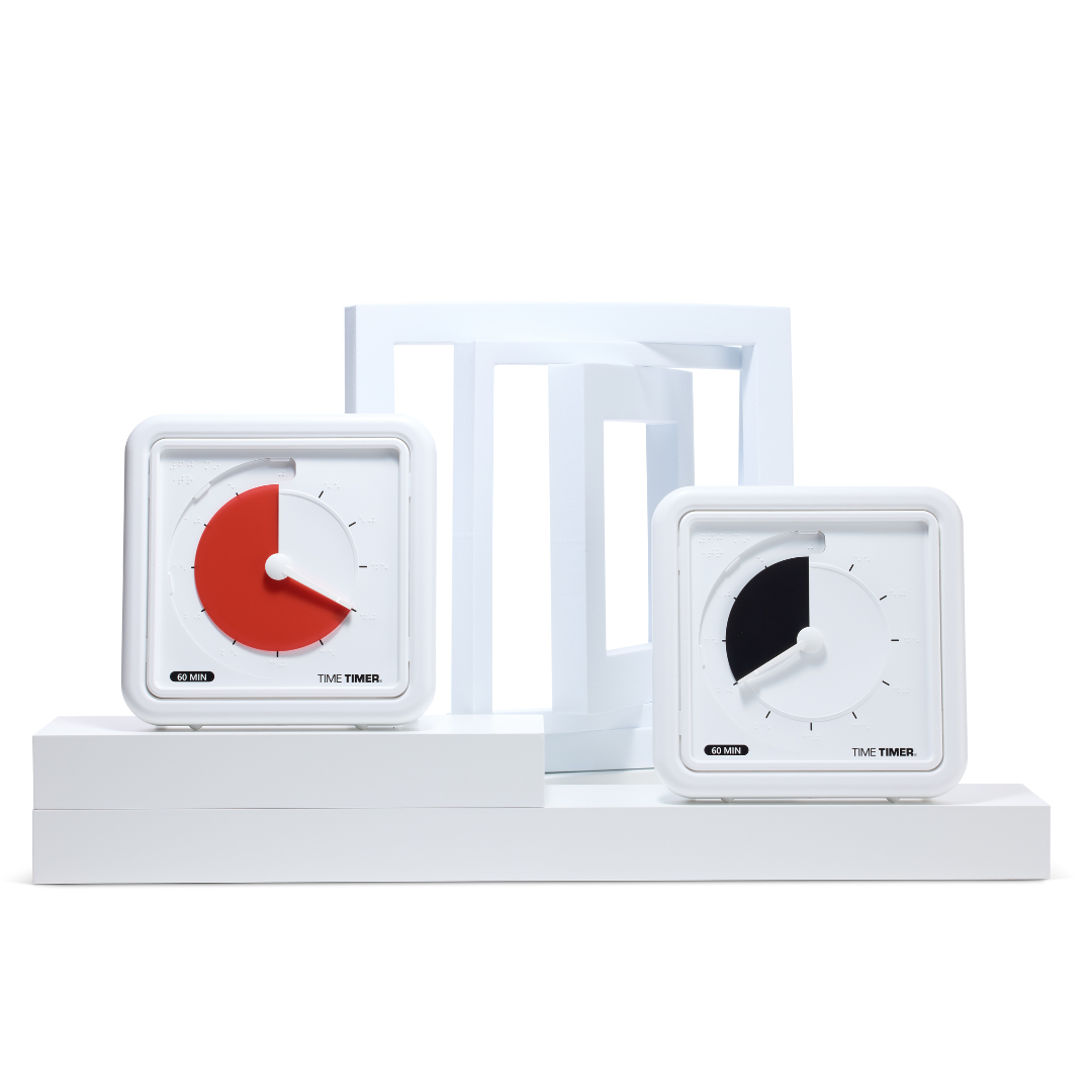 Two Time Timer Braille (8 Inch) timers by Time Timer are shown on white platforms with abstract geometric shapes. The left shows 45 minutes remaining; the right, with a black disk, displays 15 minutes.