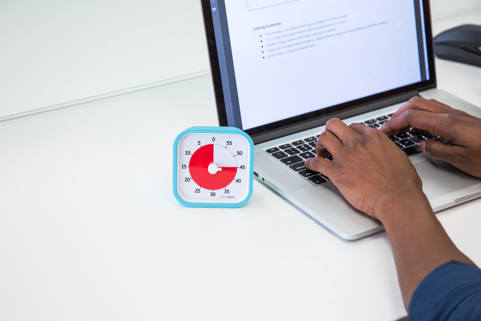 A person types on a laptop with a Time Timer MOD [Sky Blue] (60 min) by Time Timer in a silicone case nearby, showing about 20 minutes left—highlighting the use of this visual time management tool for productivity.