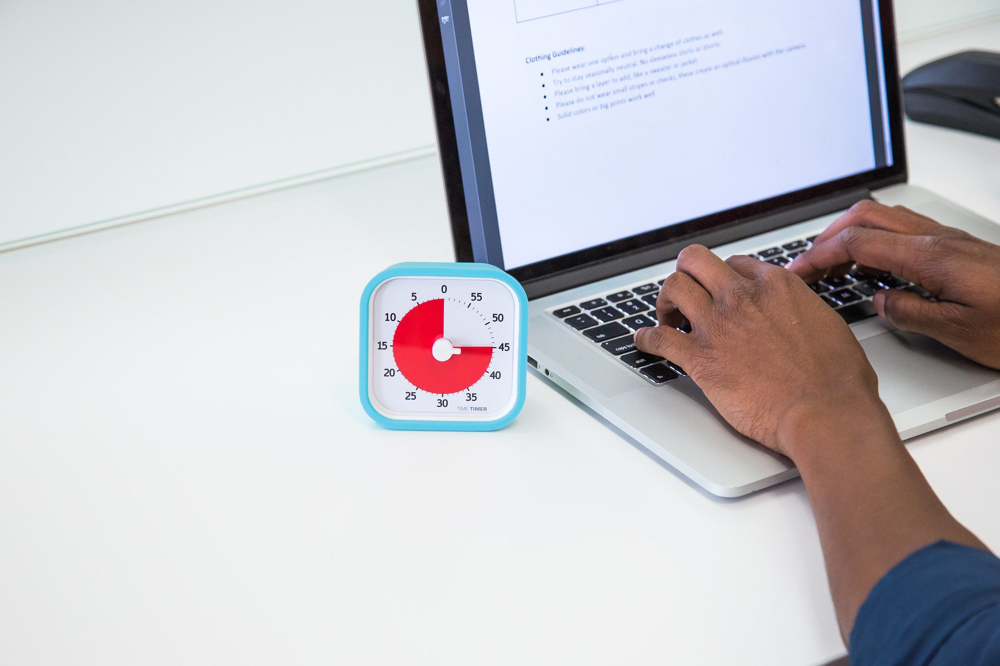 A person types on a laptop with a Time Timer MOD [Sky Blue] (60 min) by Time Timer in a silicone case nearby, showing about 20 minutes left—highlighting the use of this visual time management tool for productivity.