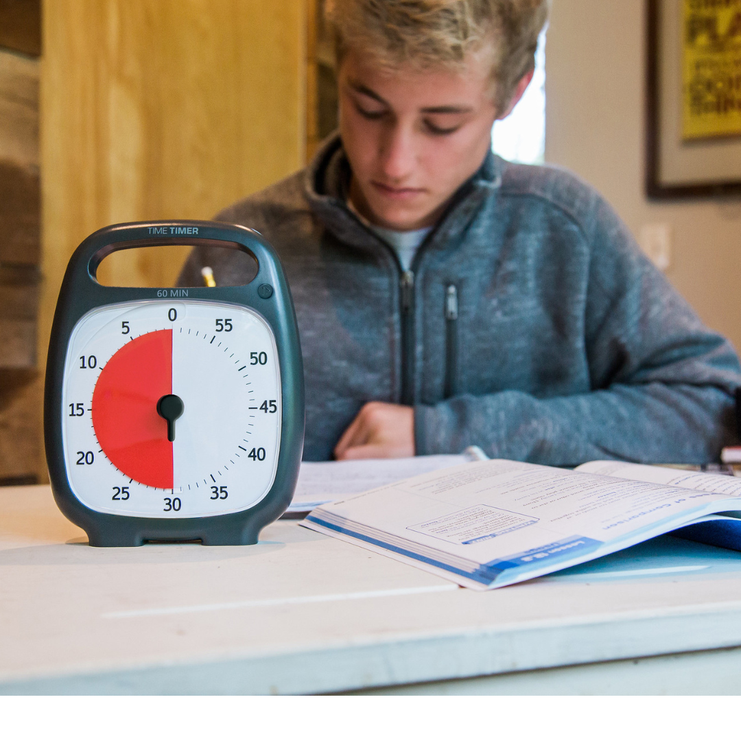 A young person studies at a desk with an open notebook. In the foreground, the Time Timer Plus (60 min) by Time Timer is set to 20 minutes, serving as a visual aid to help track study time and maintain focus.