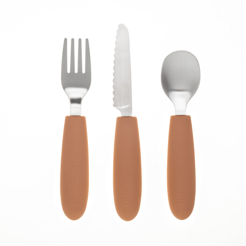 The KiddiKutter Kids Cutlery Set [Peach Fuzz] by KiddiKutter includes a fork, serrated knife, and spoon with brown silicone handles, arranged vertically side by side on a white background.
