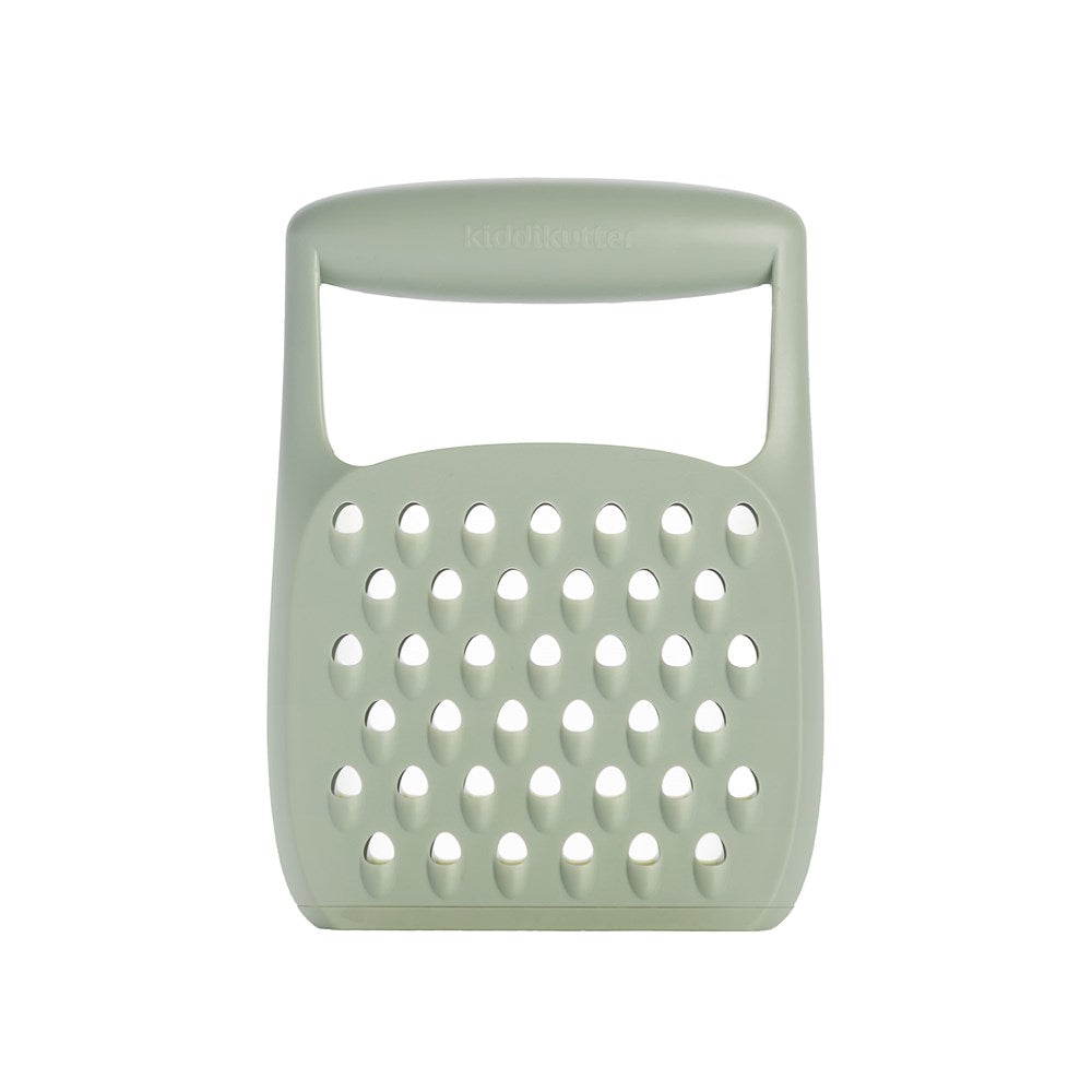 The KiddiKutter Grater by KiddiKutter is a light green, rectangular handheld food grater with a large handle and multiple oval holes, designed for kids to safely grate cheese or vegetables during meal prep.