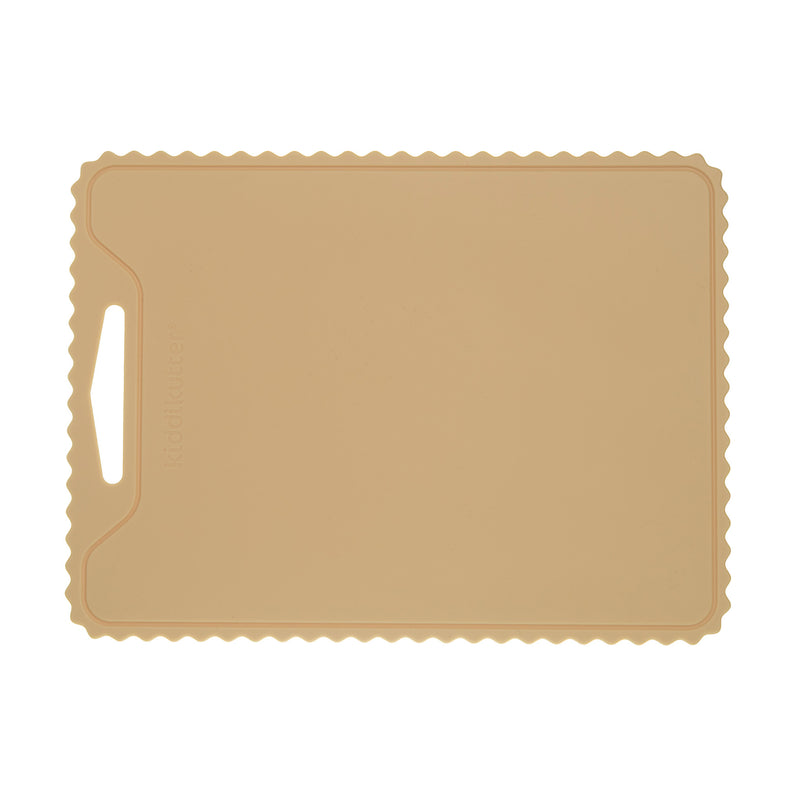 The KiddiKutter Silicone Cutting Board (Wavy) in cream by KiddiKutter features a rectangular, non-slip design with scalloped edges and a handle slot on the left, shown against a white background.
