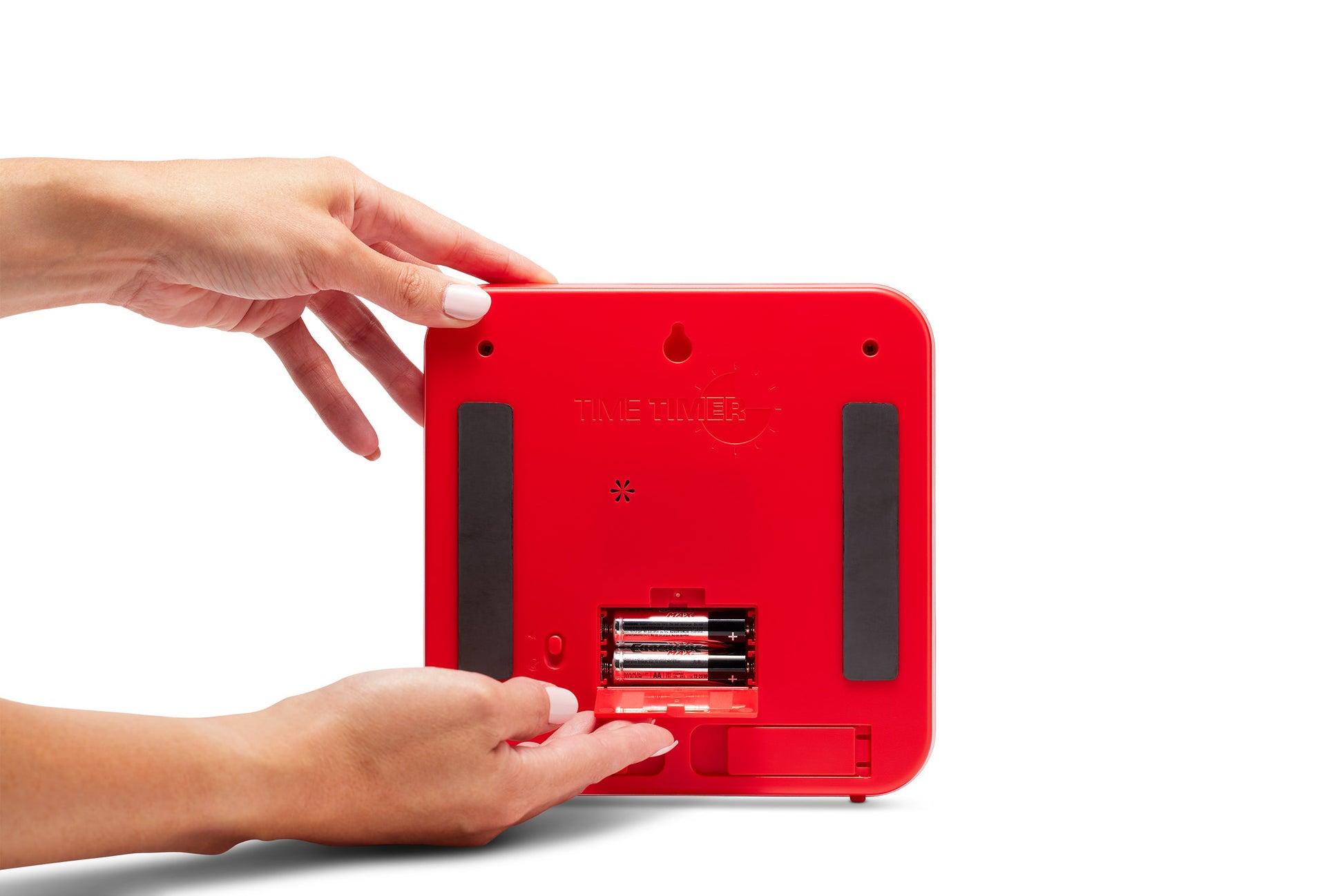 A person inserts batteries into the Time Timer Original (8 inch) Learning Center Classroom Set by Time Timer. The red square device with black grip strips and an open battery compartment is shown against a white background.
