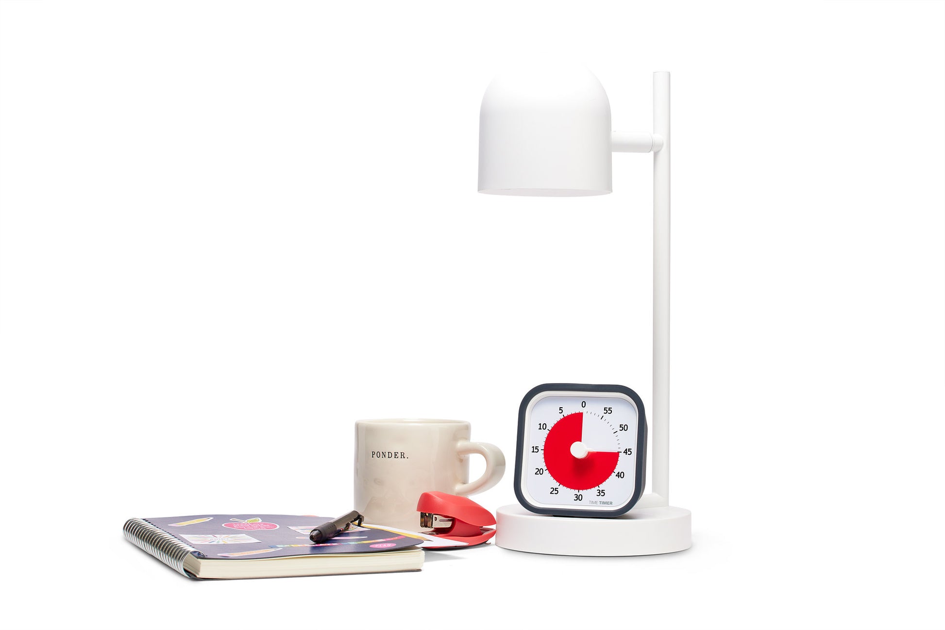 A white desk lamp, a mug labeled PAUSE., a red stapler, a Time Timer MOD [Charcoal] (60 min) from Time Timer set to 20 minutes, a notebook with colorful stickers, and a black pen on a white surface.