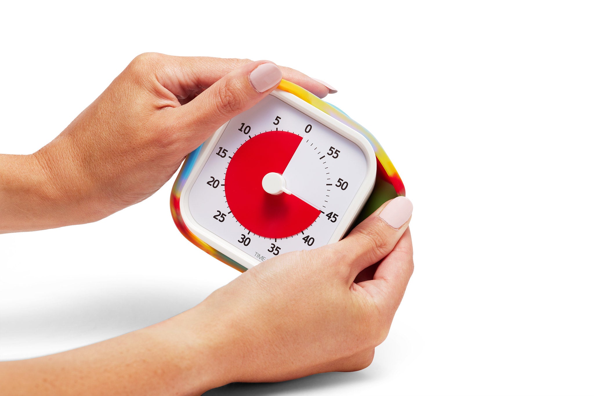 Two hands hold a Time Timer MOD [Tie Dye] (60 min) by Time Timer. Its red dial is set to 50 minutes, black numbers mark five-minute intervals on the white face, and the timer has a colorful border. The background is plain white.