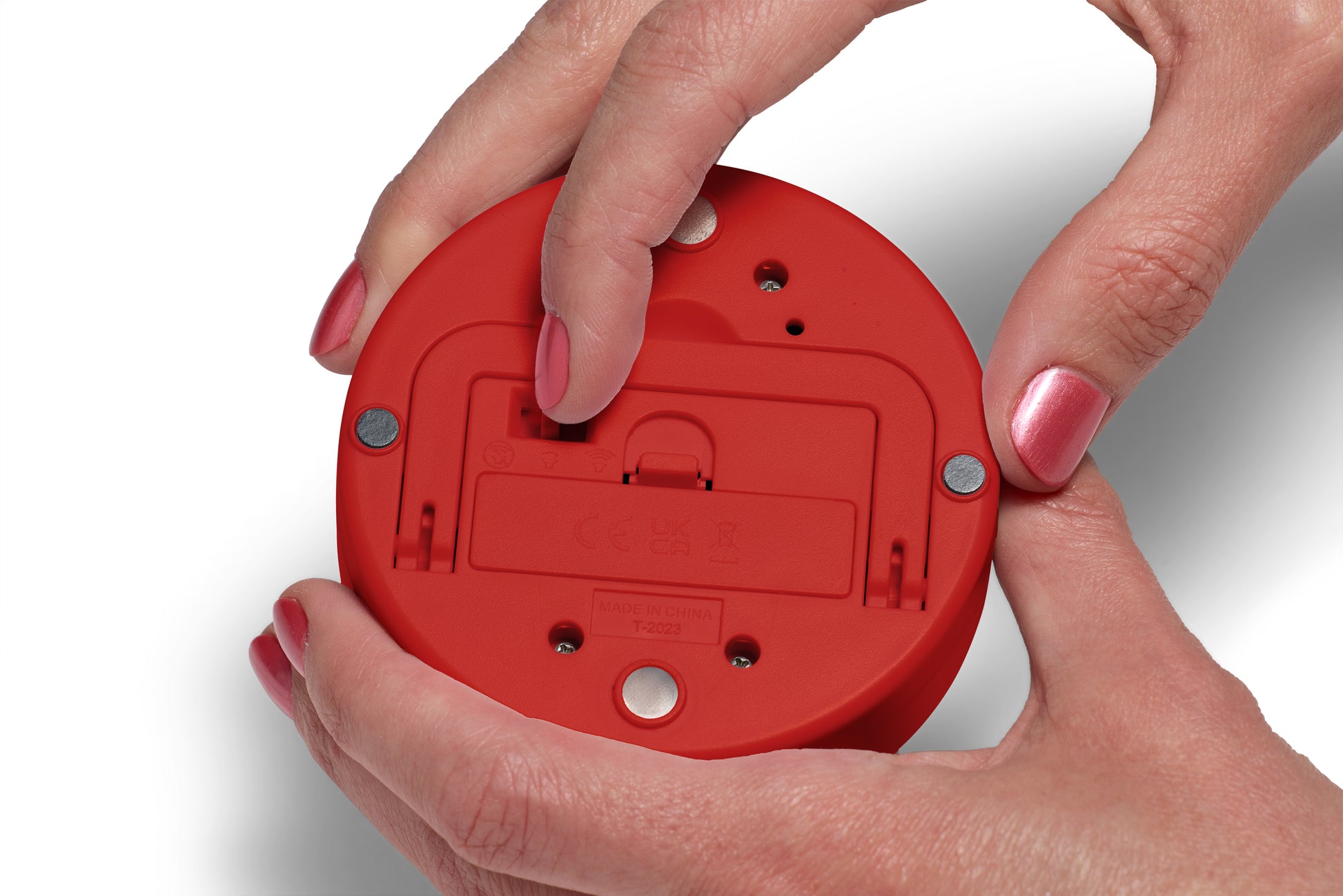 A person with pink-painted nails uses their thumb to open the battery compartment on the bottom of a round, red Time Timer Twist with Kickstand by Time Timer.