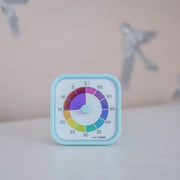 The Time Timer MOD - Home Edition [Rainbow Wheel] (60 min) by Time Timer features a light blue frame and a colorful rainbow dial, perfect for autism support. Bird illustrations appear softly blurred in the background as it rests on a white surface.