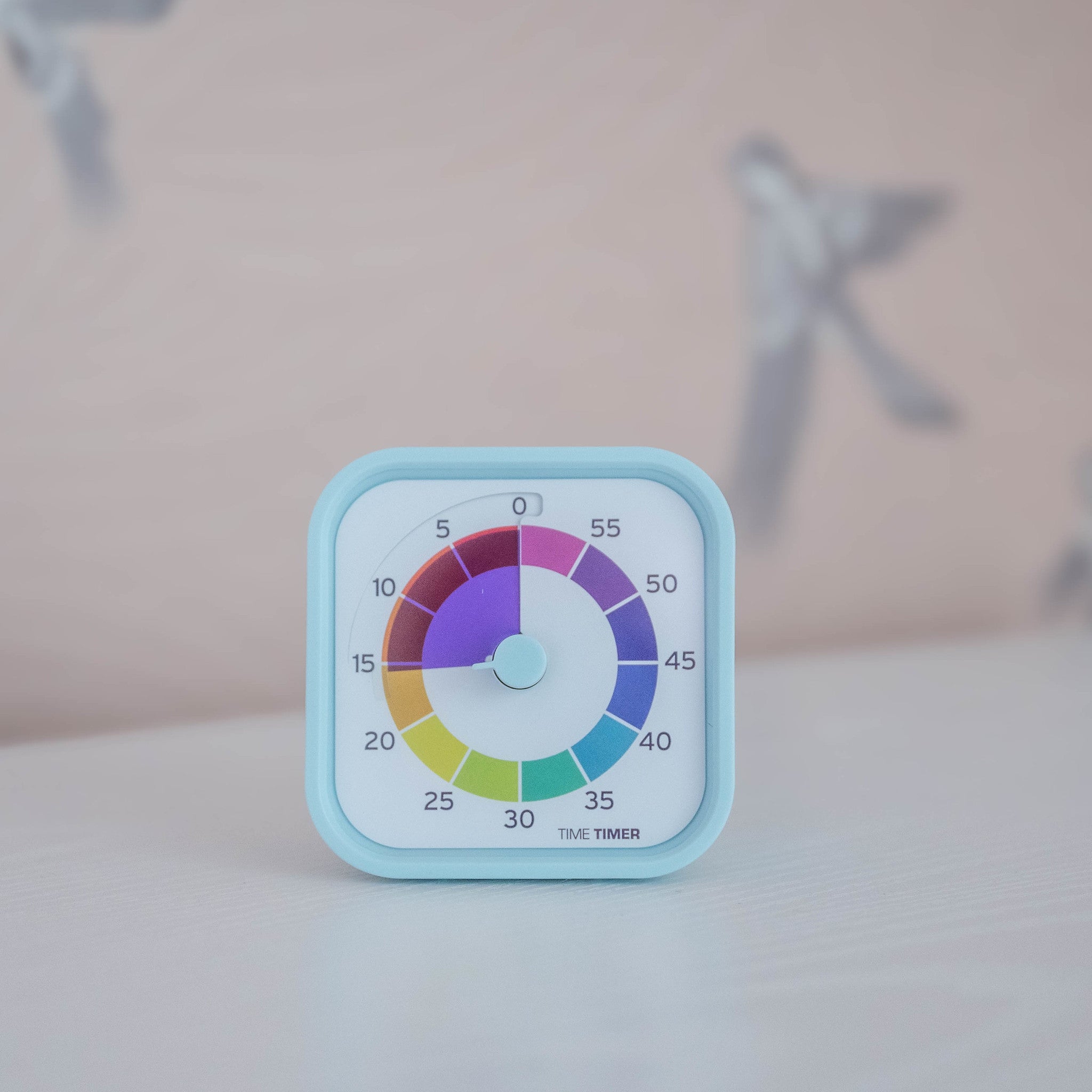 The Time Timer MOD - Home Edition [Rainbow Wheel] (60 min) by Time Timer features a light blue frame and a colorful rainbow dial, perfect for autism support. Bird illustrations appear softly blurred in the background as it rests on a white surface.