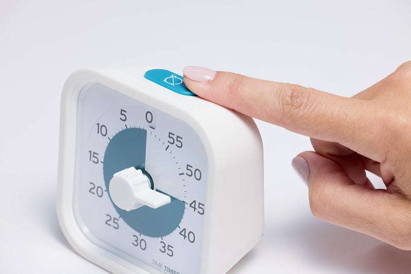 A manicured hand presses the blue button on the Time Timer PRO Applied Visual Timer (60 min) by Time Timer, featuring black numbers and a blue circular indicator—ideal for medication reminders and stylishly functional on any white surface.