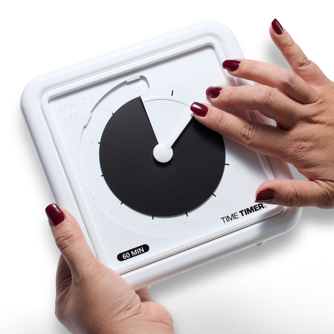A person with red painted nails sets the Time Timer Braille (8 Inch) [Black Disk] by Time Timer, a white square tactile timer labeled for accessibility, with one hand turning its large black dial while the other holds this assistive device.