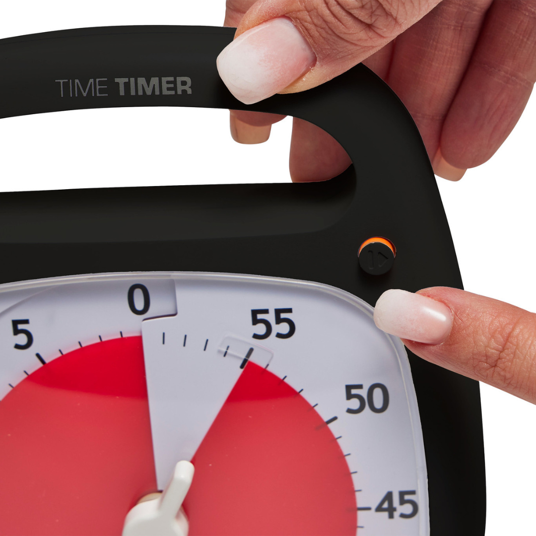 A hand holds a Time Timer Plus (60 min) by Time Timer, while another presses a button next to the clock face, which displays about 44 minutes left in red—a handy tool for staying focused and managing time effectively.
