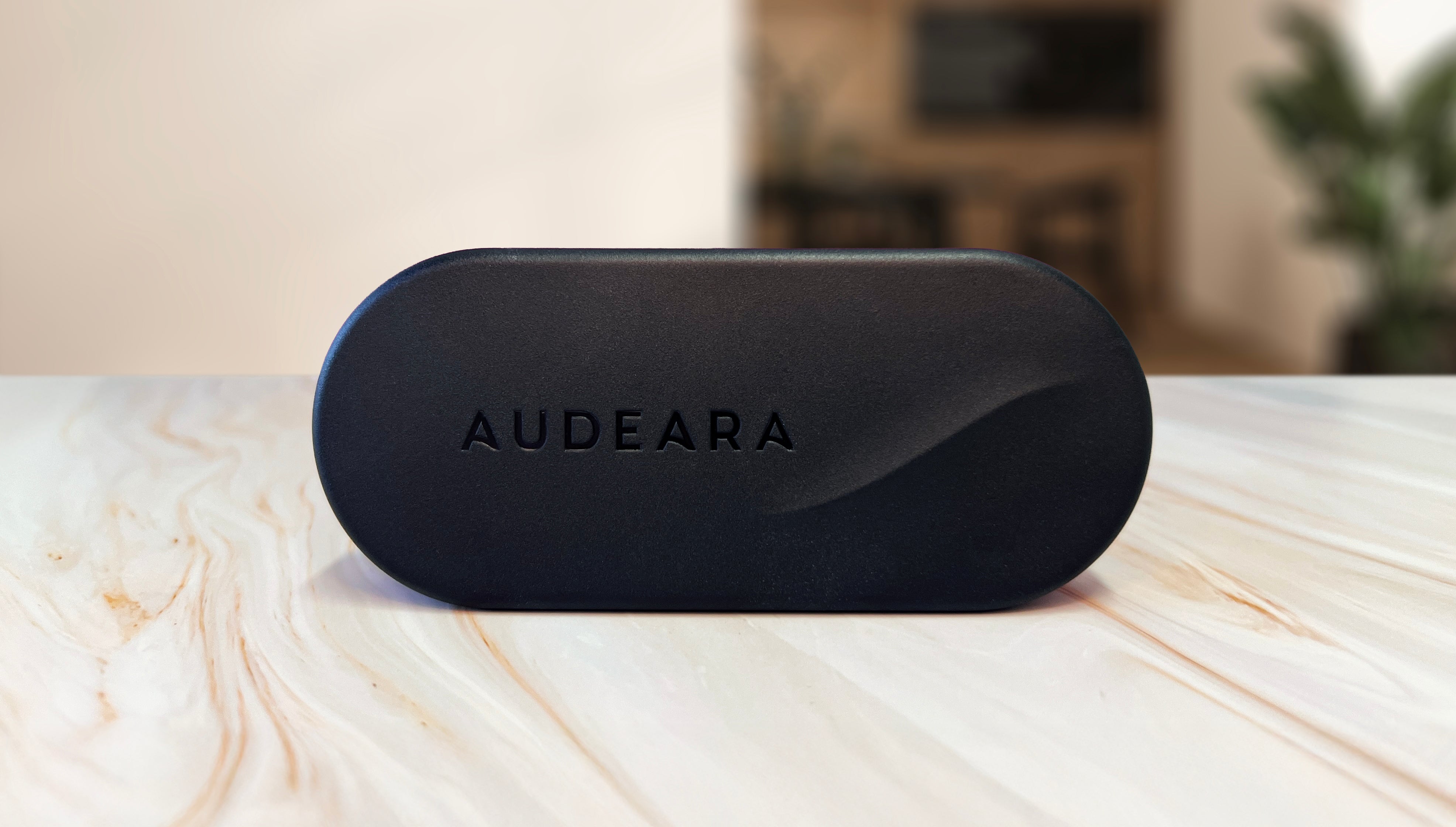 A black, oval-shaped case with AUDEARA embossed on it rests on light marble, promoting the Audeara Broadcaster (Auracast™ Transmitter)—an advanced audio solution for inclusive listening by Audeara.