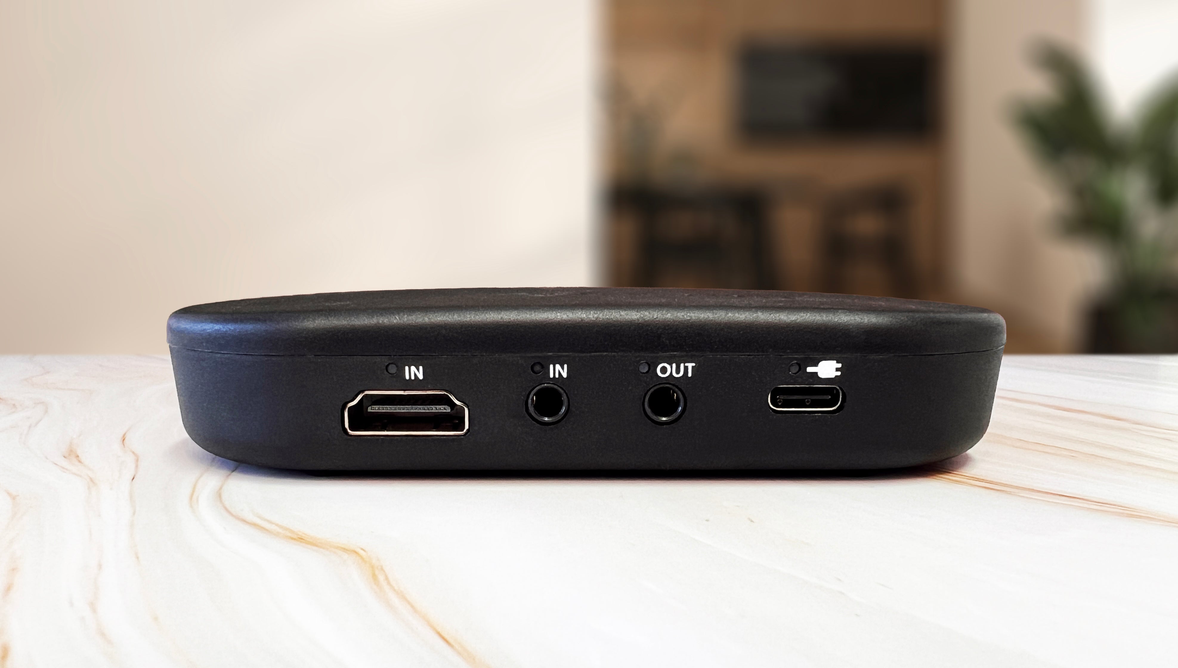 The Audeara Broadcaster (Auracast™ Transmitter) by Audeara, featuring HDMI IN, two audio jacks (IN/OUT), Auracast technology, and a USB-C port, rests on a light surface with a blurred indoor background.