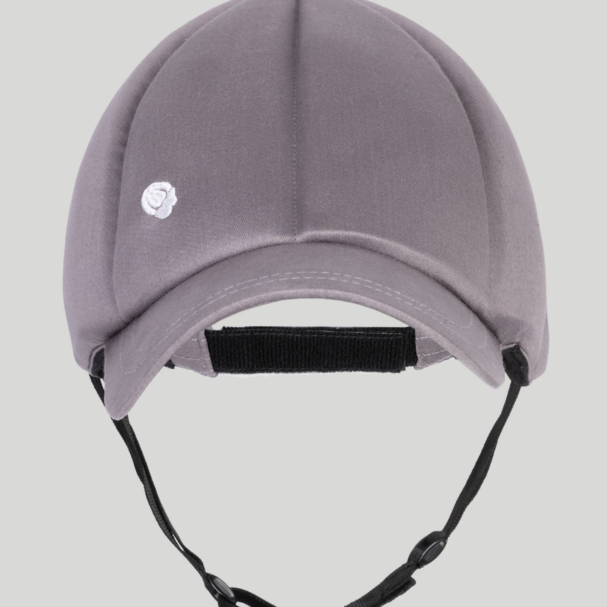 The Ribcap Baseball Cap [Platinum] by Ribcap is a gray padded medical helmet with a short brim, adjustable chin strap, and a small white logo on the front left. Perfect for soft head protection and NDIS assistive technology needs. Plain light gray background.