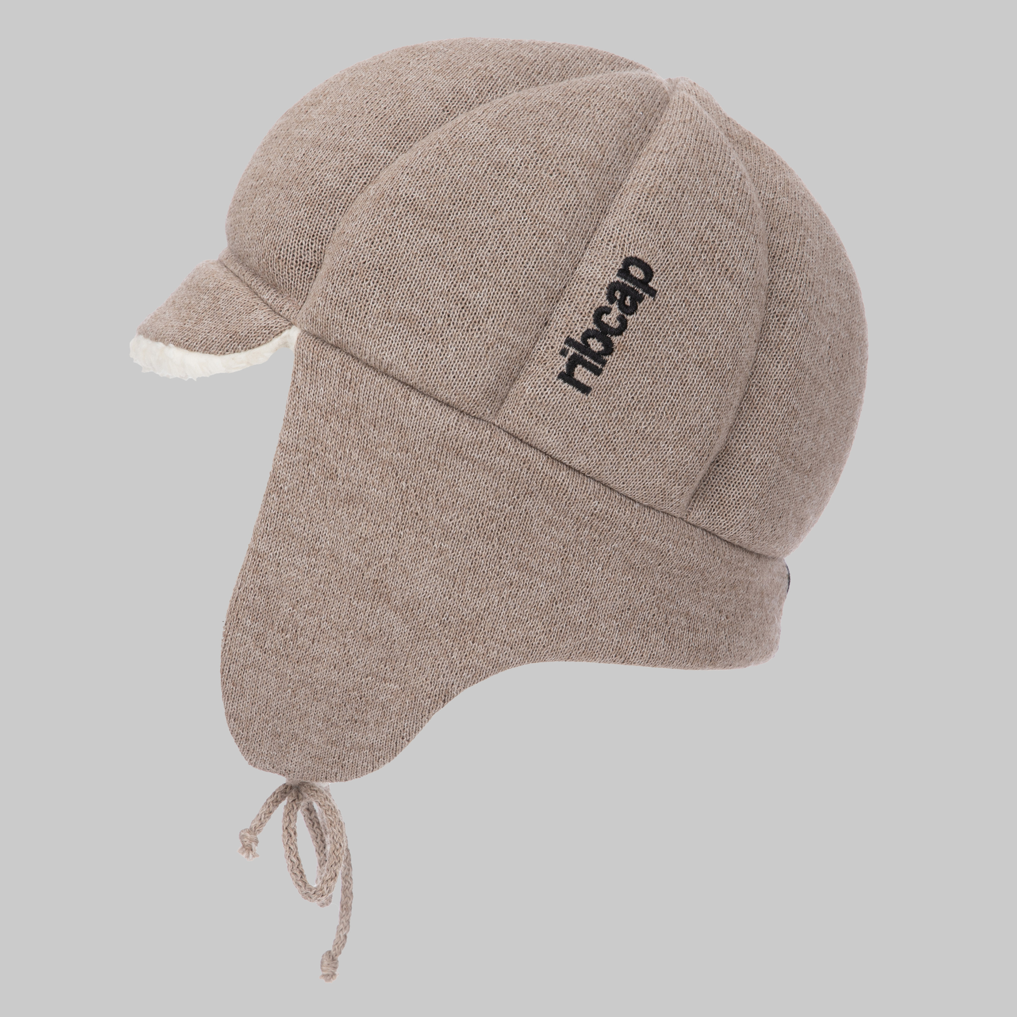 The Ribcap Bieber Kids Beanie [Brown] by Ribcap is a beige knit winter hat with ear flaps, white fleece lining, chin ties, and "ribcap" embroidered in black—designed for kids’ head protection as a stylish assistive accessory.