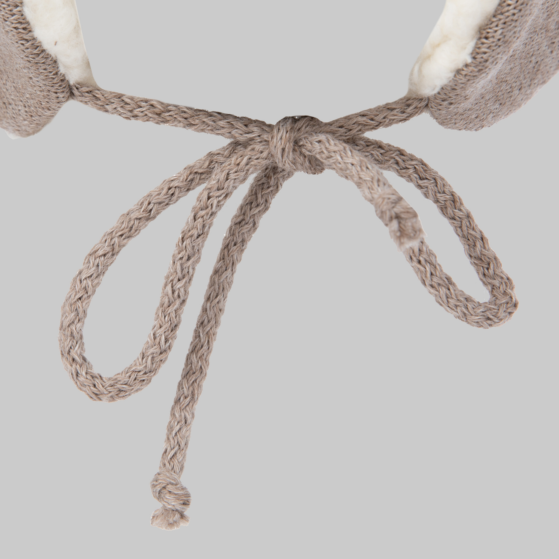Close-up of a beige knitted bow on the Ribcap Bieber Kids Beanie [Brown] helmet by Ribcap, featuring soft, light-colored fabric at the top, set against a plain gray background.