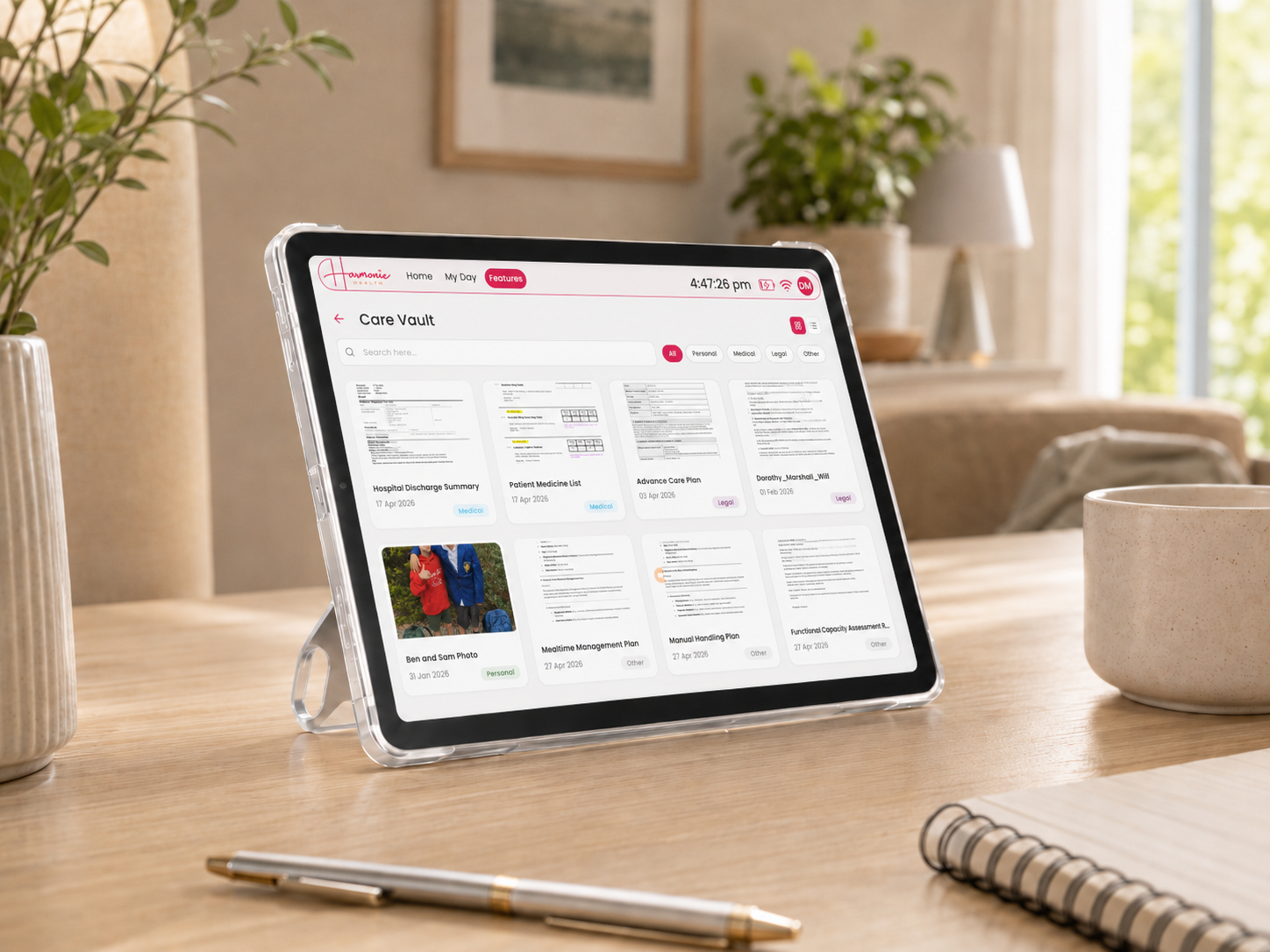 A Harmonie Health Hub with Subscription by Harmonie Health is on a wooden table beside a mug, notebook, pen, and plants in a bright, modern room, displaying its digital health management app on the screen.