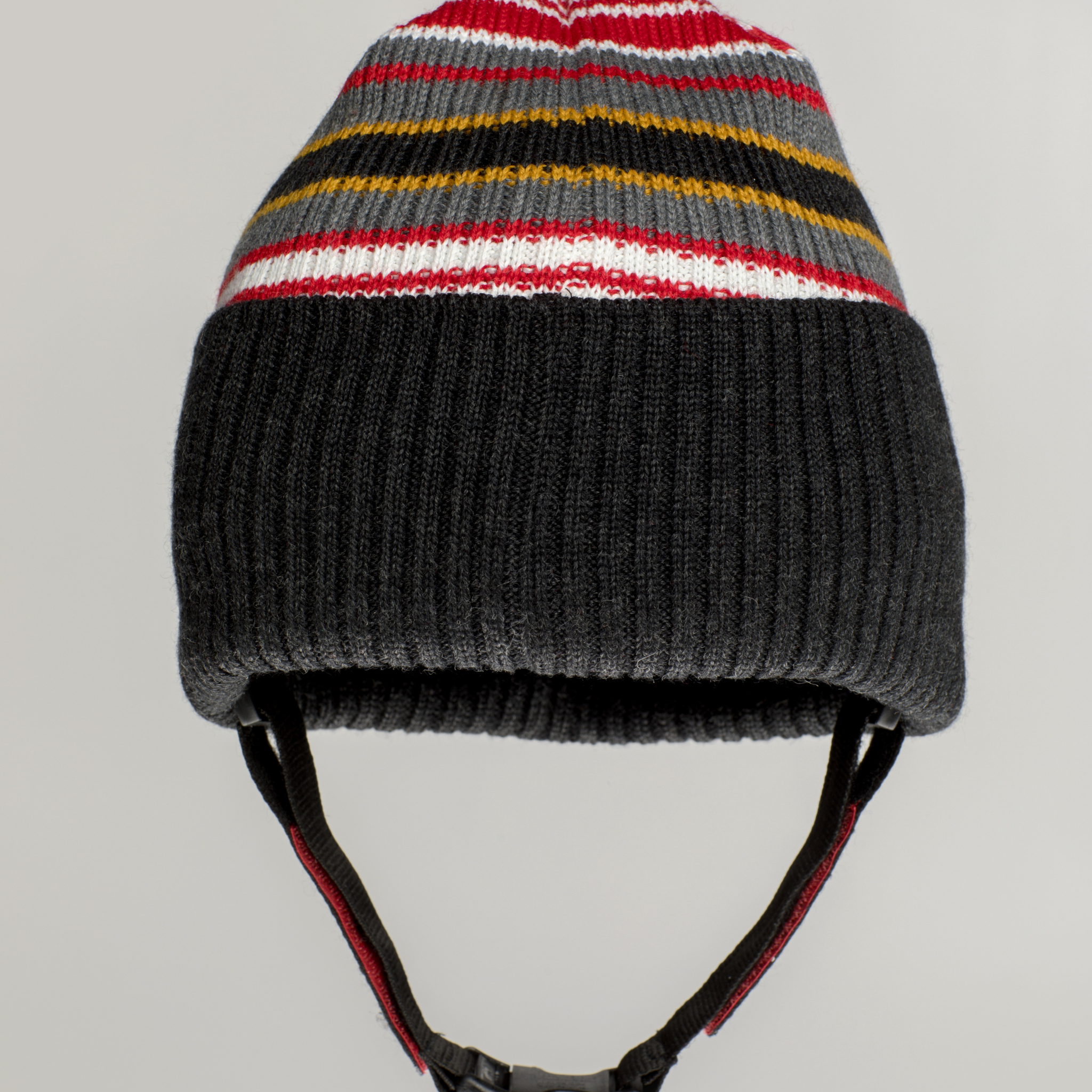 The Ribcap Iggy Beanie Protective Helmet [Stripy] by Ribcap features black ribbed ear flaps, a chin strap, and red, white, yellow, and gray stripes for stylish warmth and head protection on winter days.