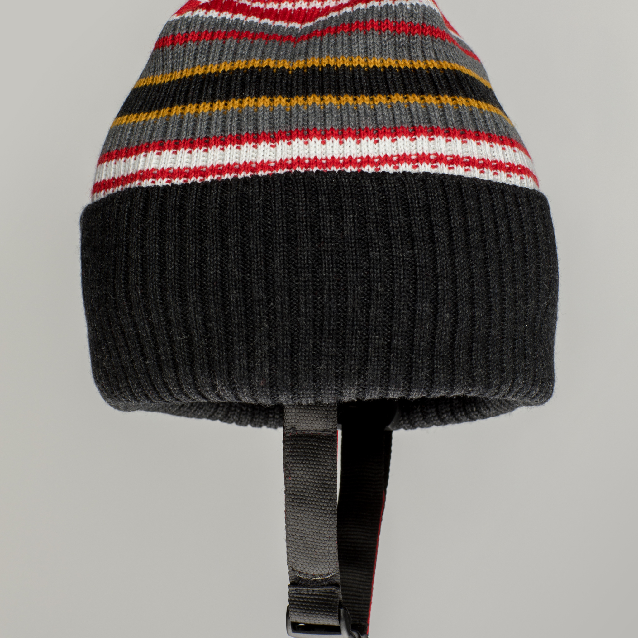 The Ribcap Iggy Beanie Protective Helmet [Stripy] by Ribcap features horizontal red, white, yellow, and gray stripes, a thick black ribbed band at the bottom, and an adjustable chin strap for comfort and security.