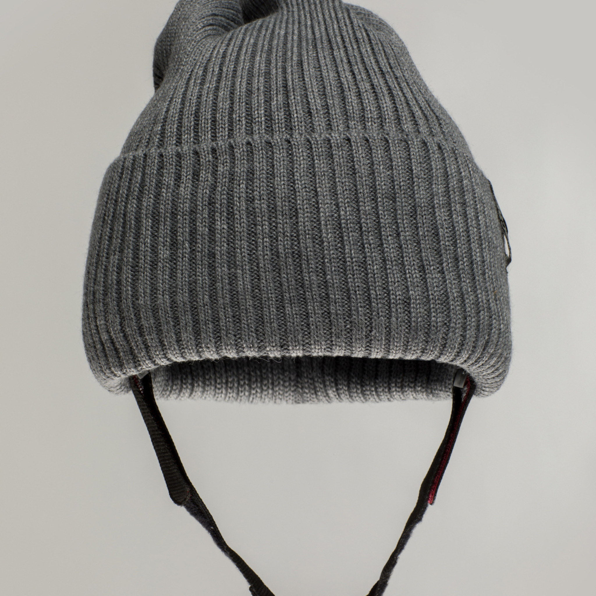 The Ribcap Lenny Beanie Protective Helmet [Grey] by Ribcap is a gray ribbed knit adult beanie with ear flaps and black adjustable straps, shown against a plain light background.
