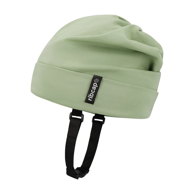 The Ribcap Lenny Summer Protective Helmet [Khaki] by Ribcap is a light green beanie with a black label and adjustable black chin straps, offering soft head protection. Displayed against a plain white background.