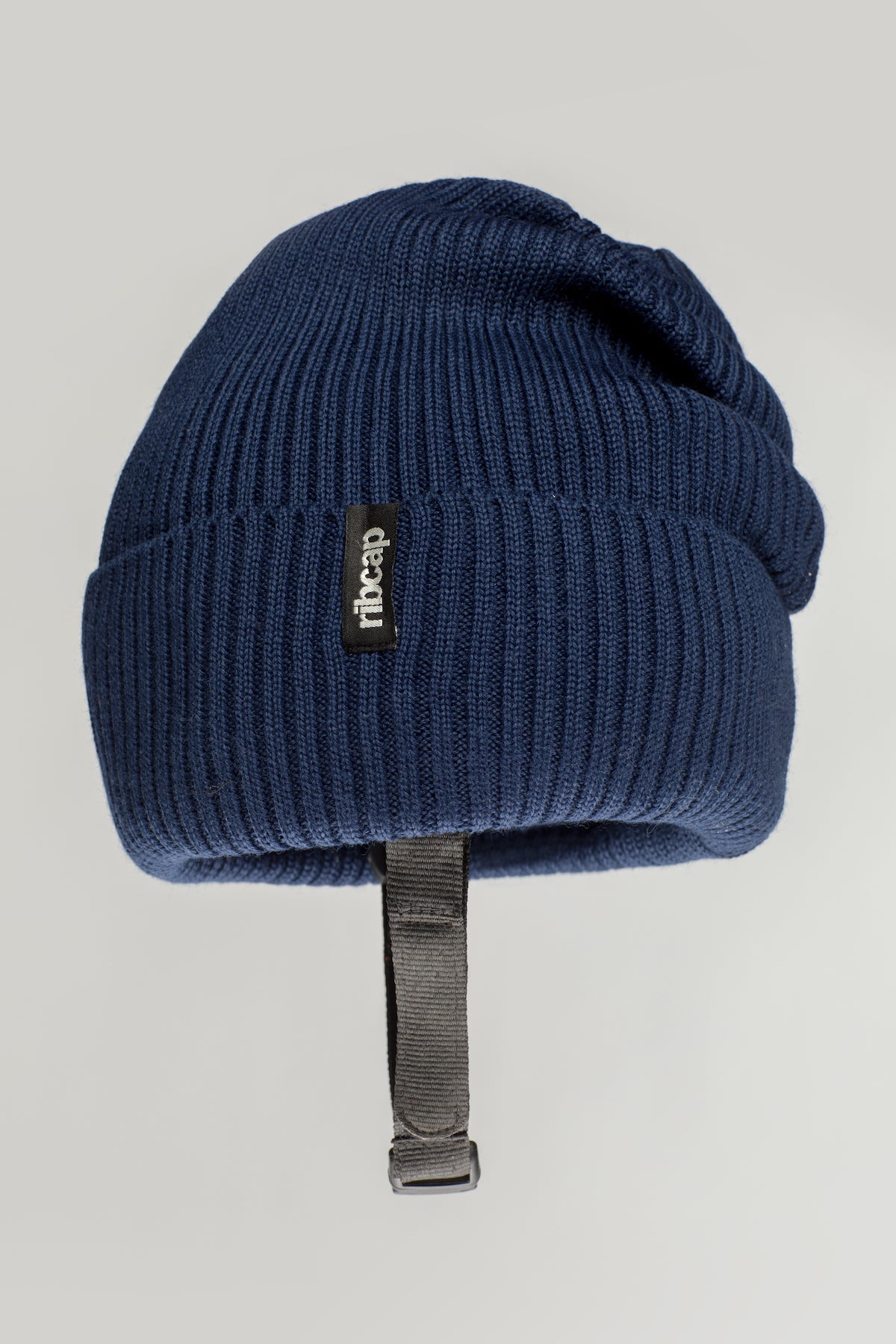 The Ribcap Lenny Beanie Protective Helmet [Marine] is a dark blue ribbed knit protective beanie by Ribcap, featuring a black stitched tag and adjustable black chin strap, shown on a plain light background.