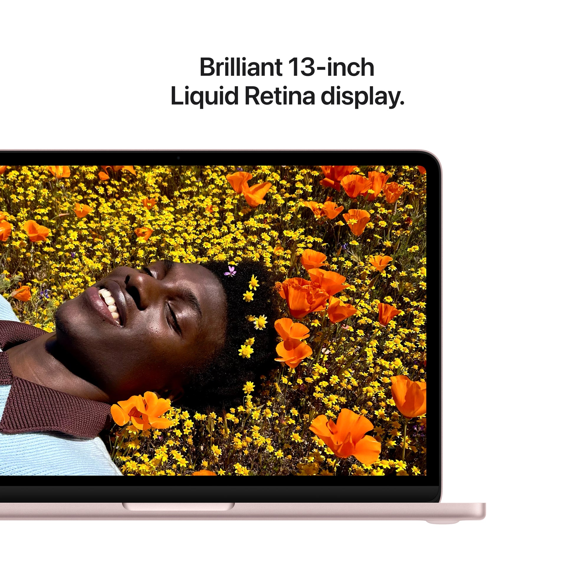 A closeup of the Apple MacBook Neo’s brilliant 13-inch Liquid Retina display shows a person lying in orange flowers, smiling with yellow blossoms in their hair. Text above reads: Brilliant 13-inch Liquid Retina display.