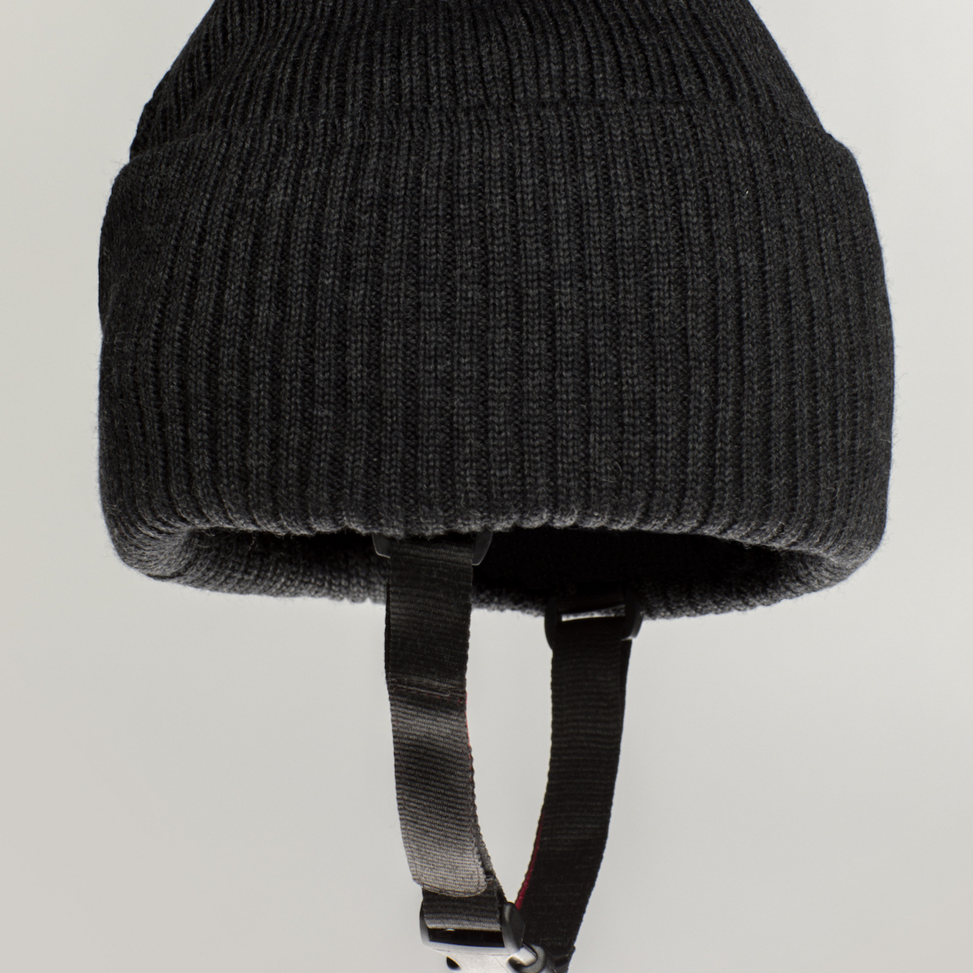 The Ribcap Lenny Beanie Protective Helmet [Anthracite] by Ribcap is a black ribbed knit beanie with attached black chin straps, inspired by soft protective helmet designs, shown against a plain light background.