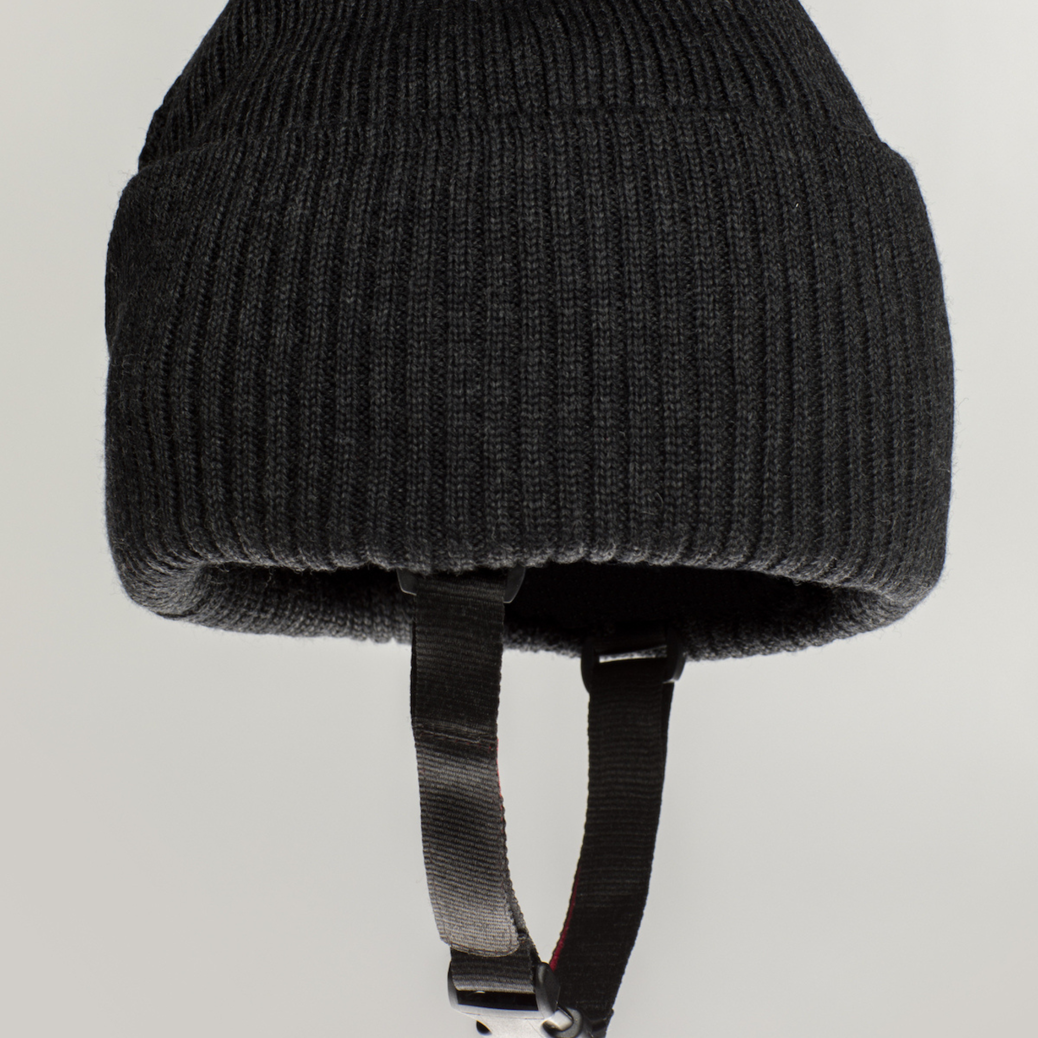 The Ribcap Lenny Beanie Protective Helmet [Anthracite] by Ribcap is a black ribbed knit beanie with attached black chin straps, inspired by soft protective helmet designs, shown against a plain light background.