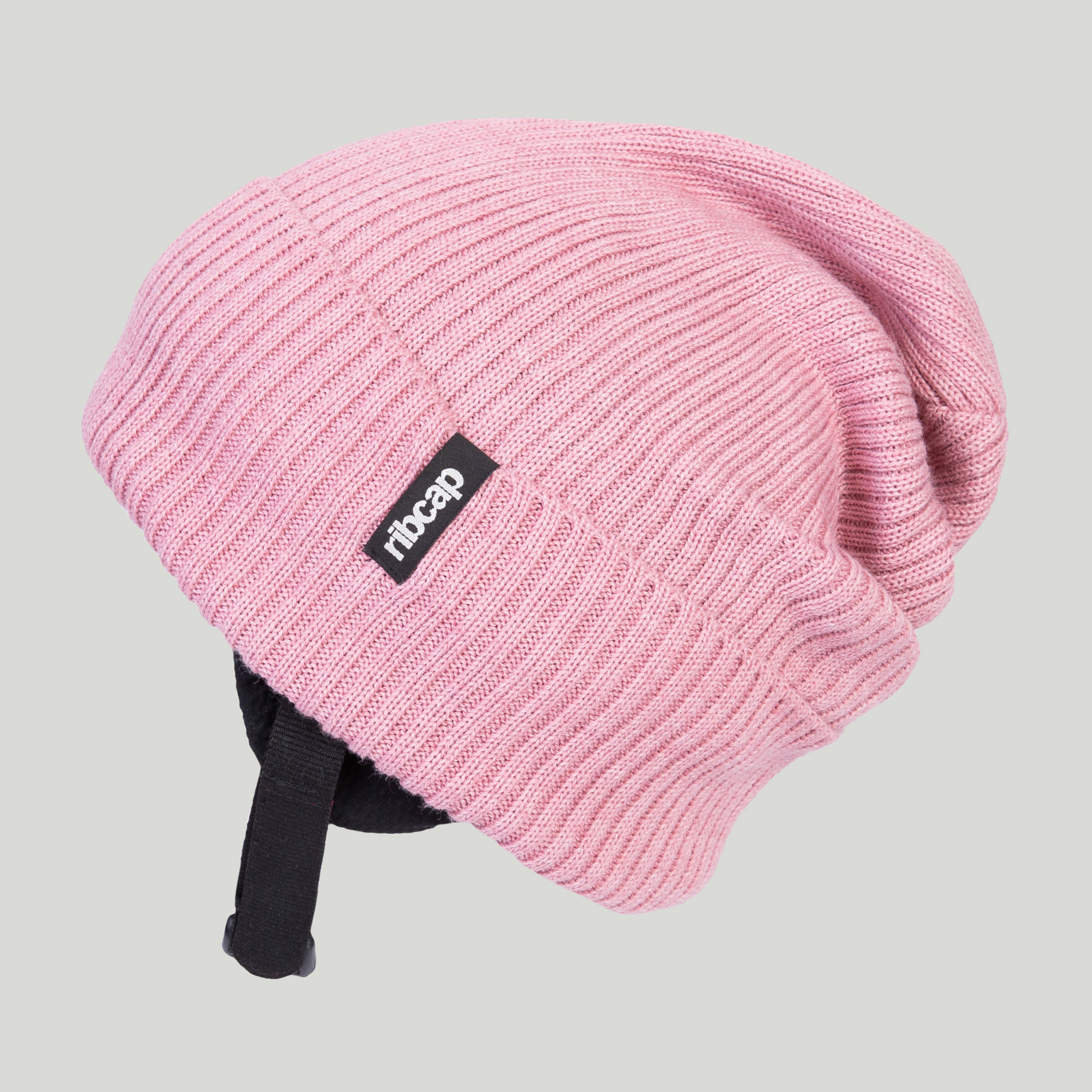 The Ribcap Lenny Beanie Protective Helmet [Rose] is a pink ribbed knit beanie with black adjustable straps and a black-and-white Ribcap tag, designed for soft head protection and shown on a neutral background.