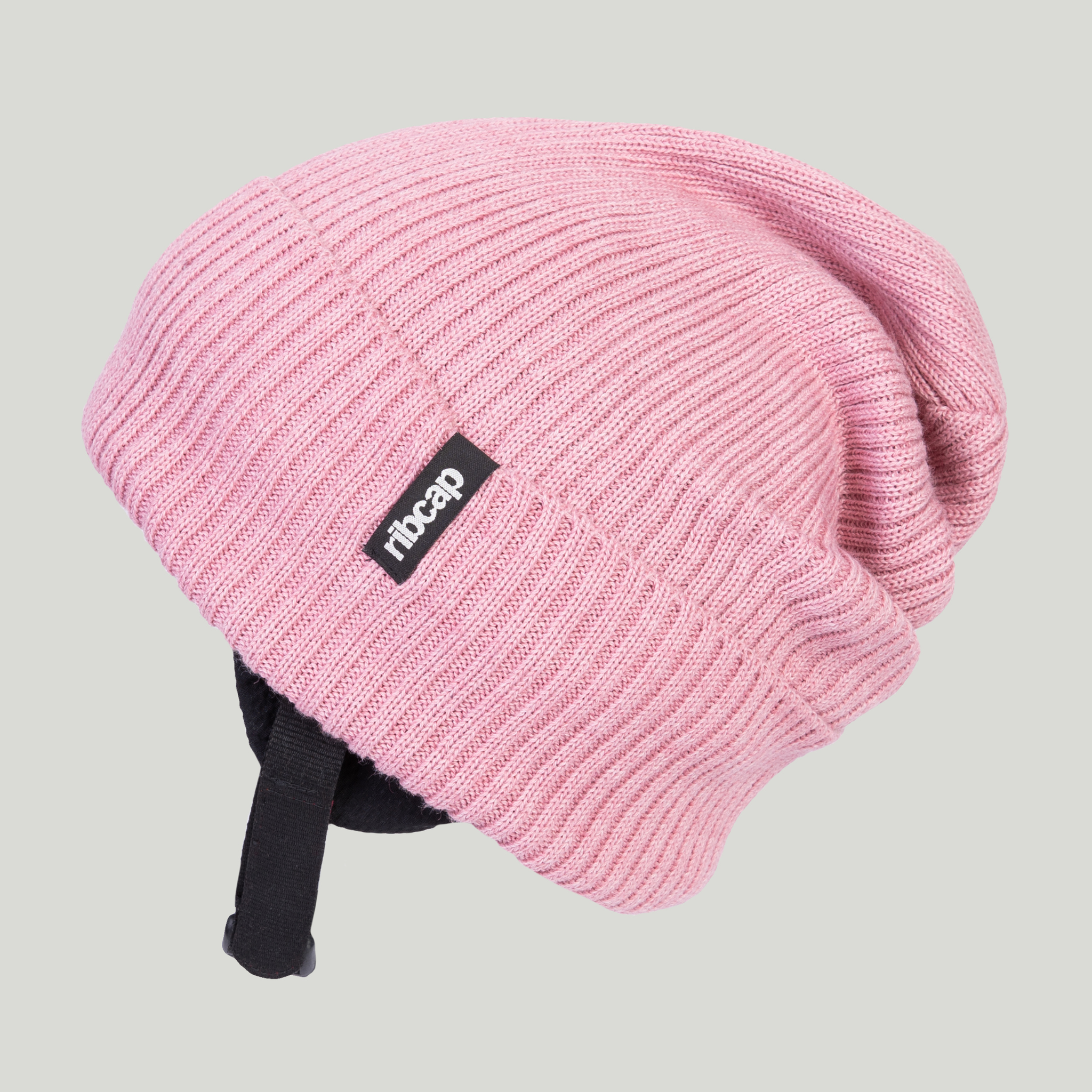 The Ribcap Lenny Beanie Protective Helmet [Rose] is a pink ribbed knit beanie with black adjustable straps and a black-and-white Ribcap tag, designed for soft head protection and shown on a neutral background.