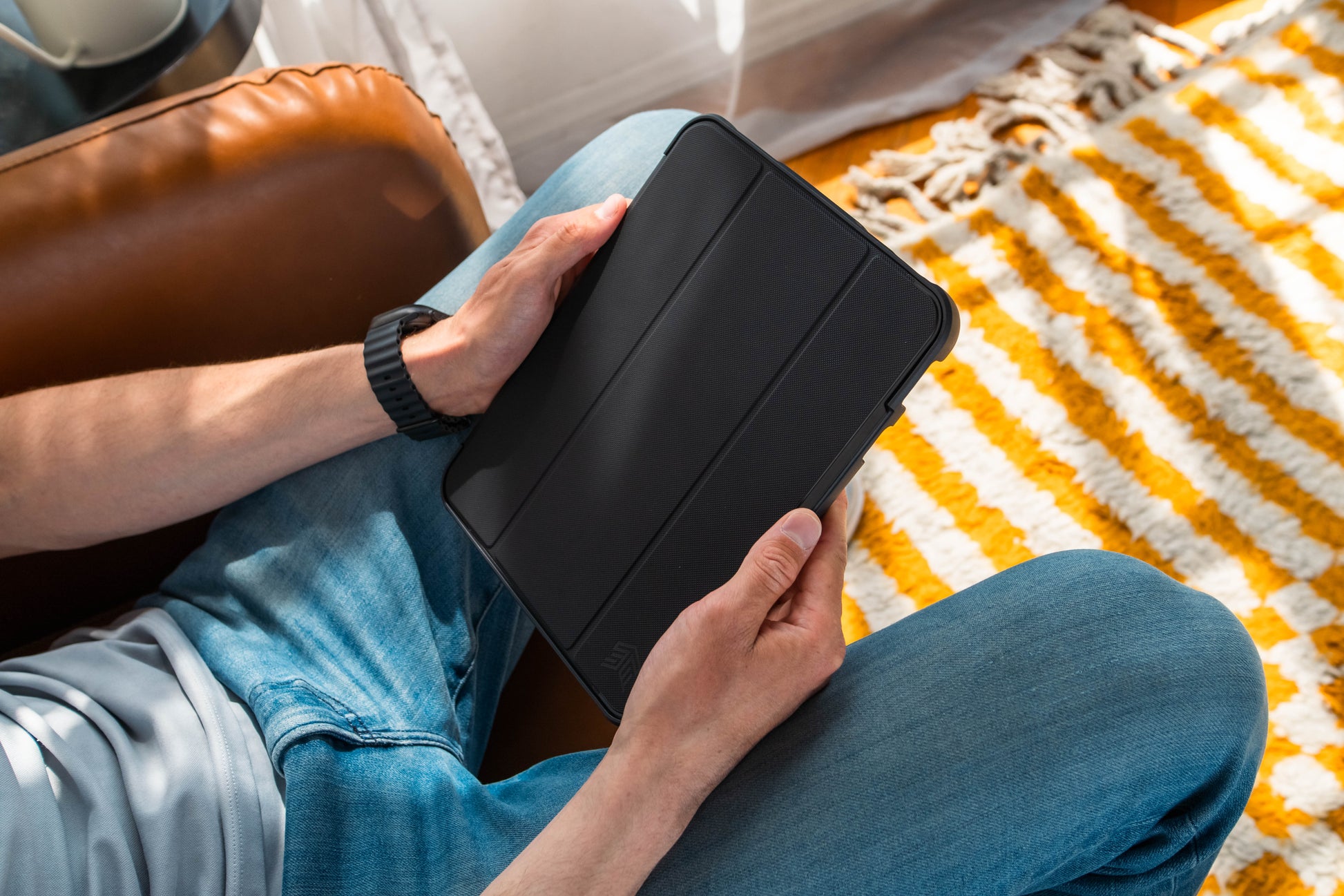 Person holding a black tablet case on a patterned rug