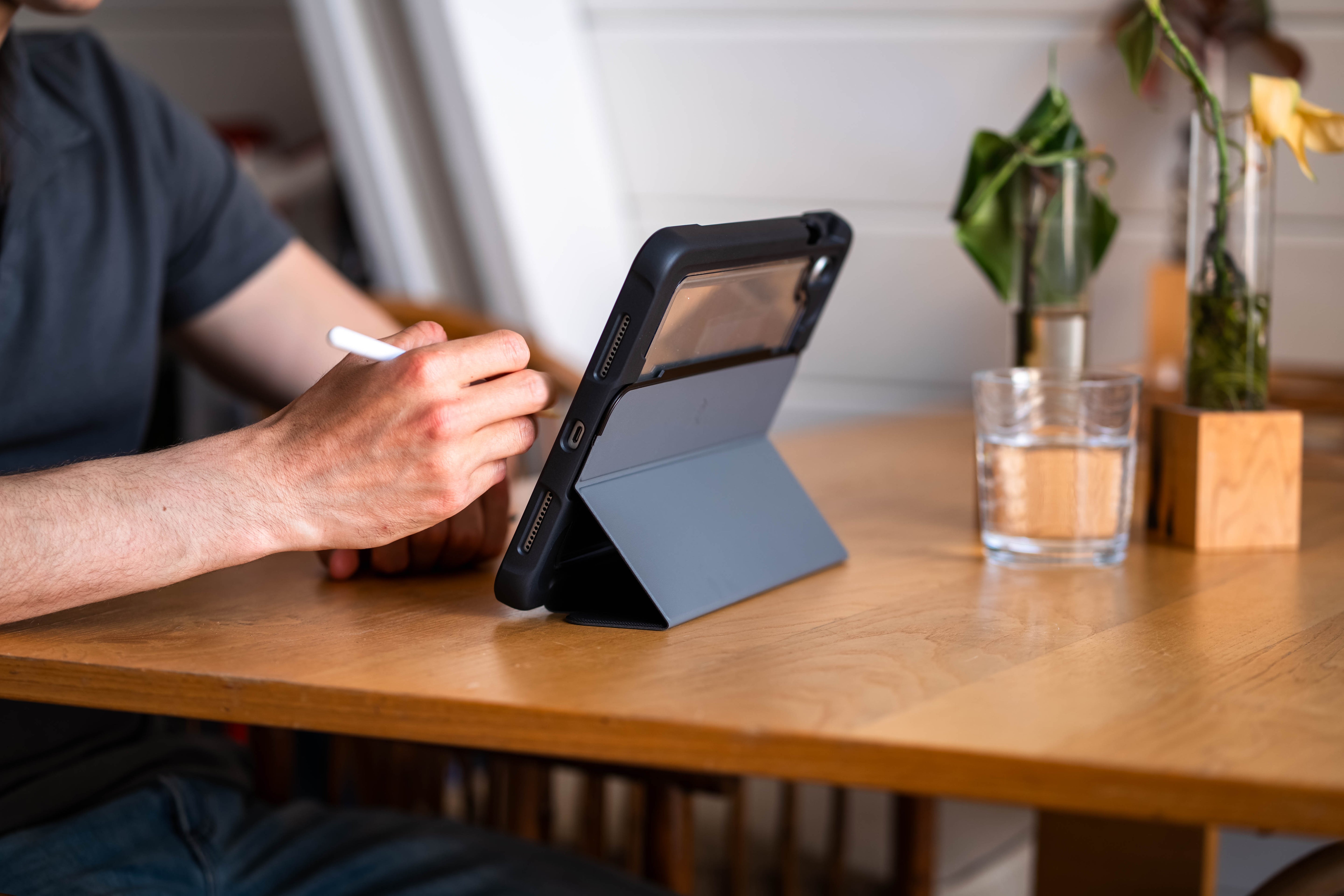 Person using a stylus on a tablet with a glass of water and plant in the background