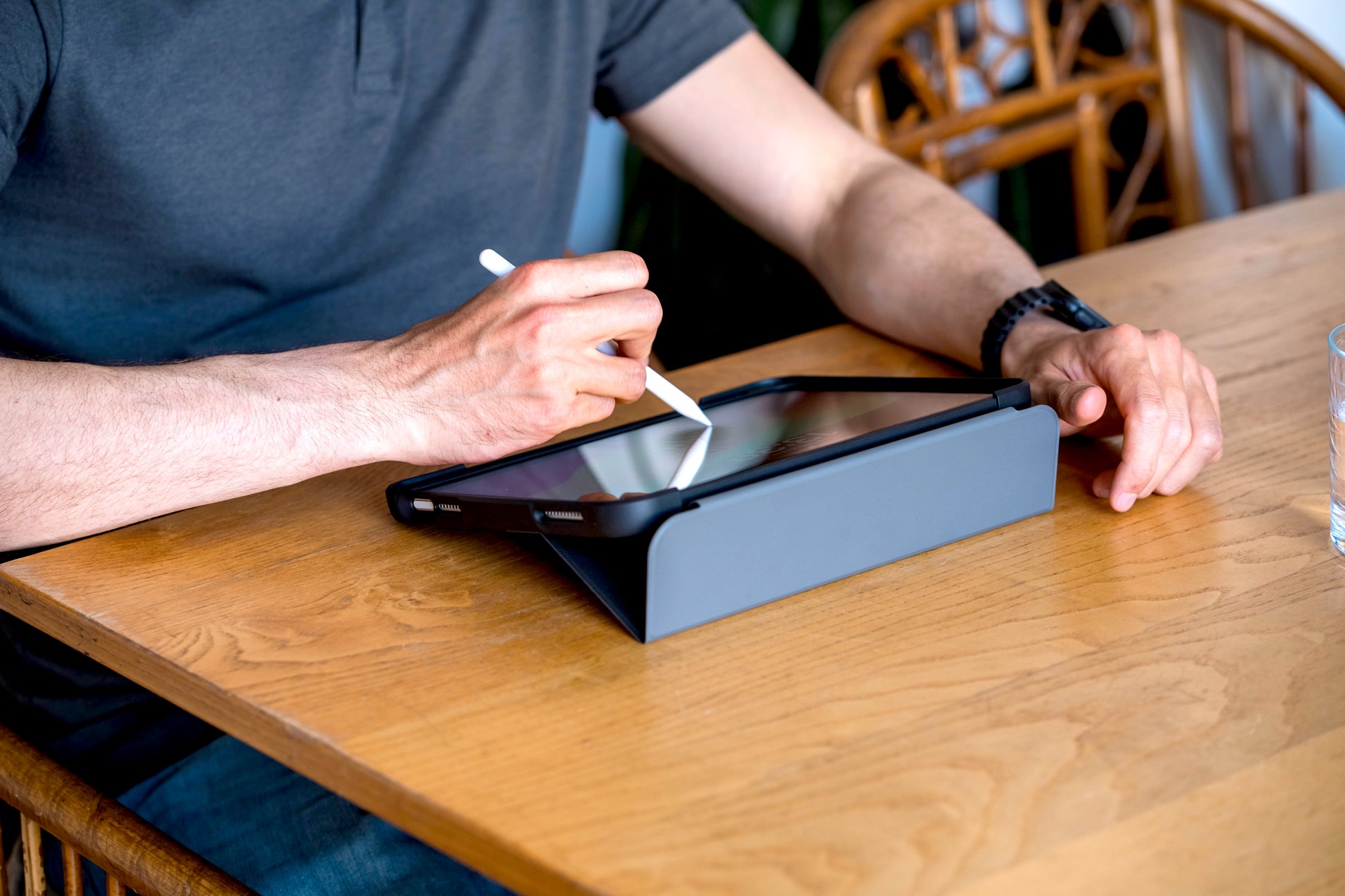 Person using a stylus on a tablet at a wooden table