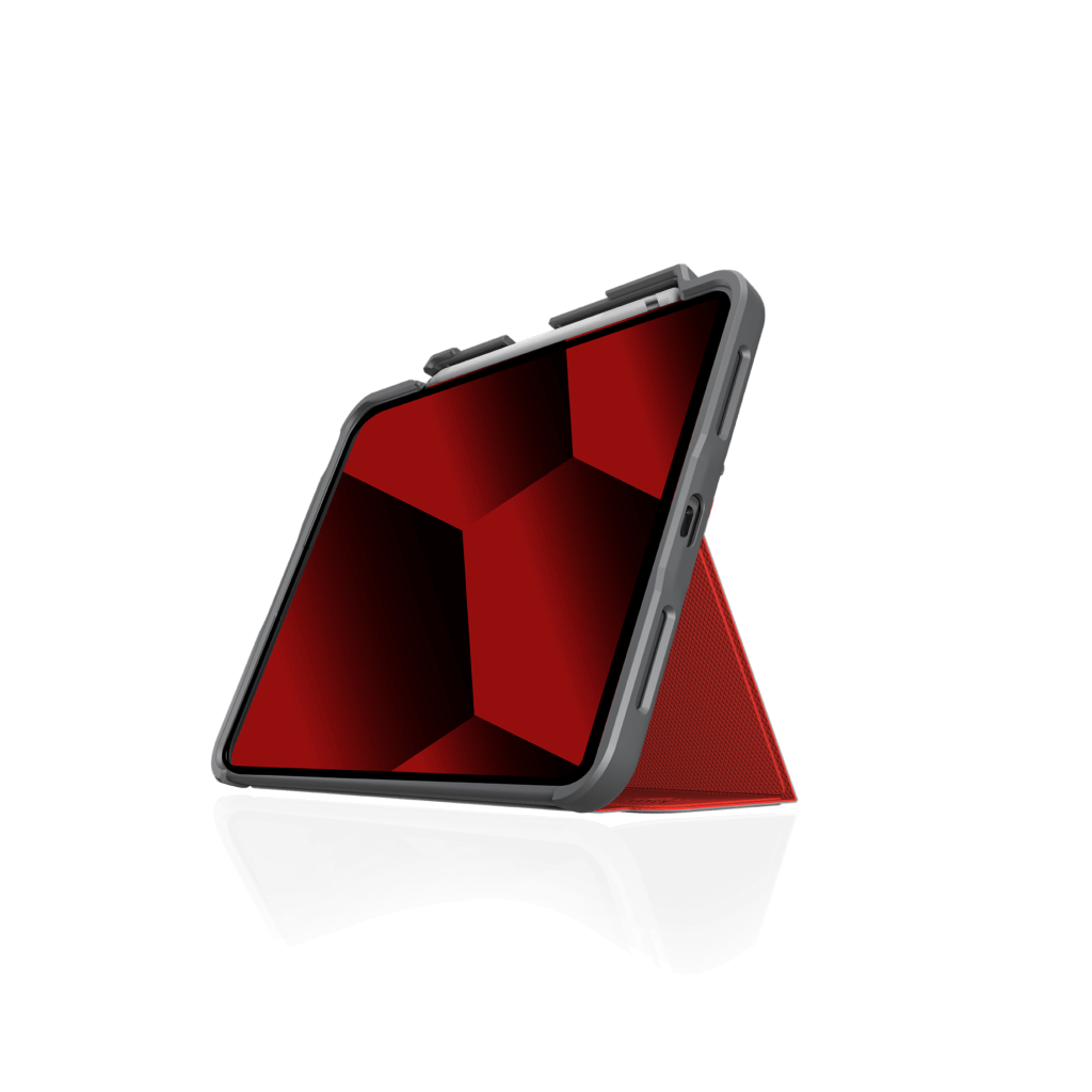 An iPad in the STM Dux Plus Case [Red] (for iPad A16/10th/11th Gen) by STM is propped in landscape. Its screen shows a geometric red and black pattern on white, while the rugged case provides military-grade drop protection.