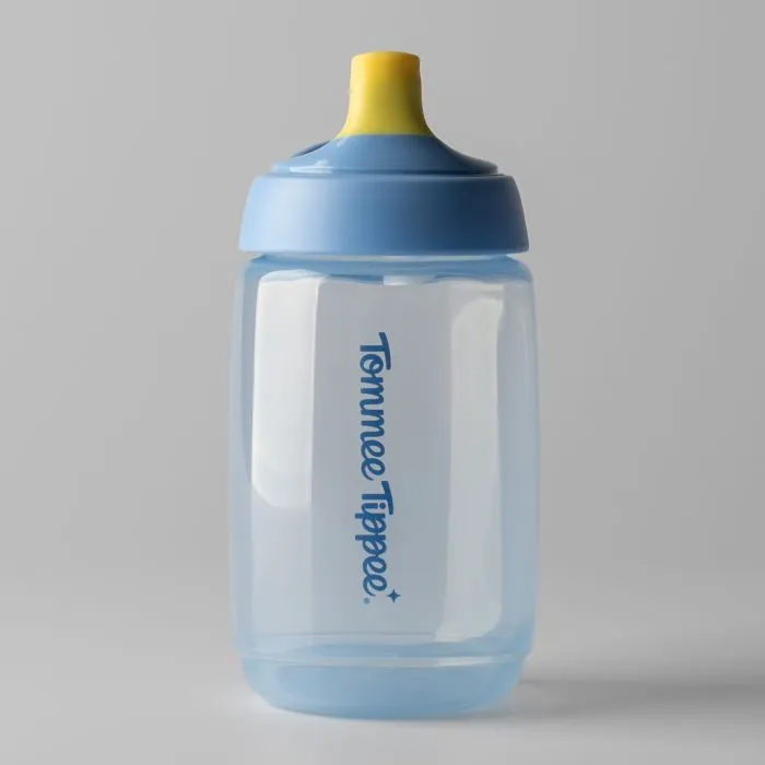 A Tommee Tippee Active Spout Cup 390mL in blue with a yellow, bite-proof spout and blue lid sits upright on a light gray background. The leak-proof cup features the brand name printed vertically on its side.
