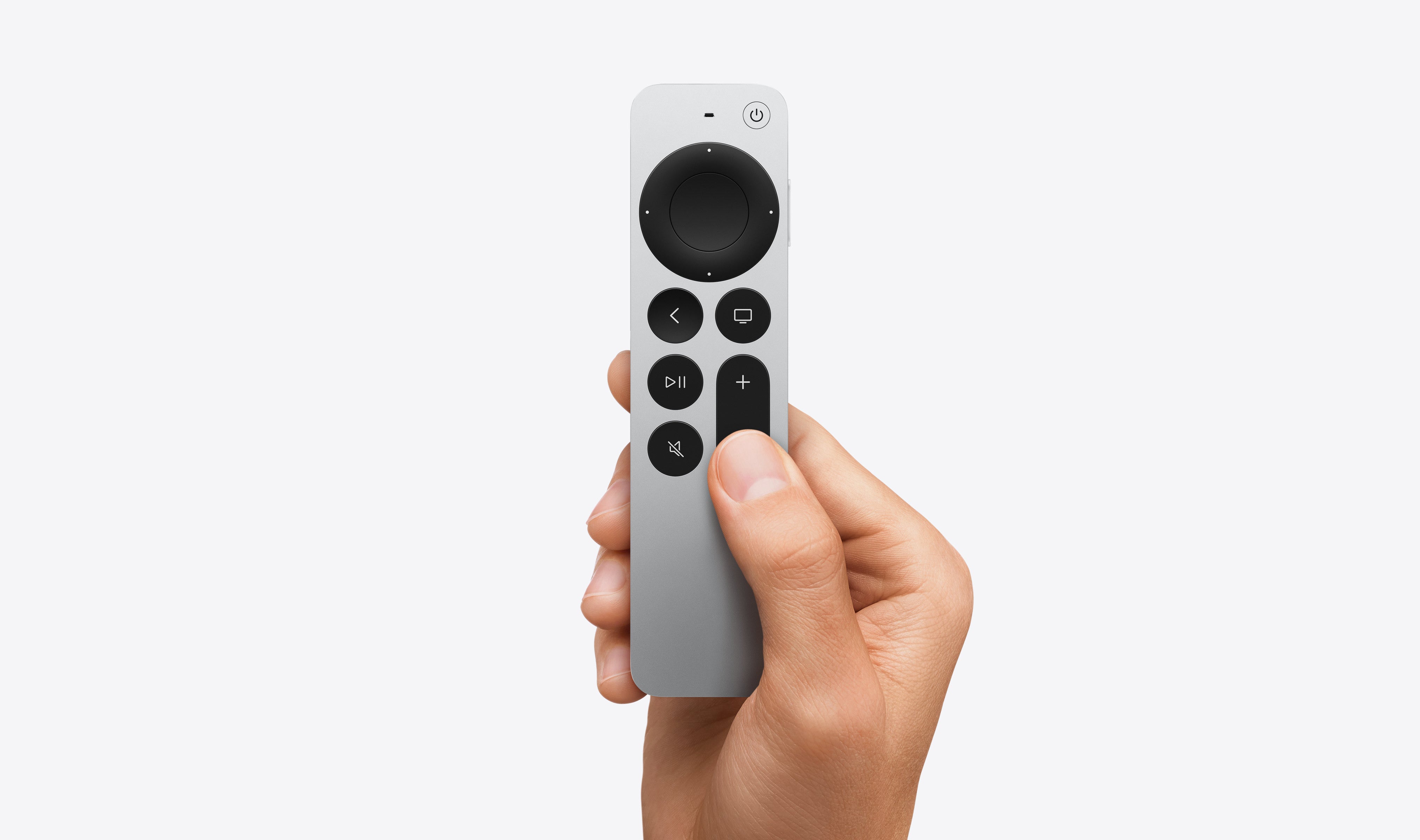 A hand holds a silver Apple TV 4K Wi-Fi+Ethernet (3rd Gen) remote with circular touchpad and black buttons for play, pause, mute, volume, and menu. Shown with HDMI & USB-C Cable Bundle from Apple against a plain light background.
