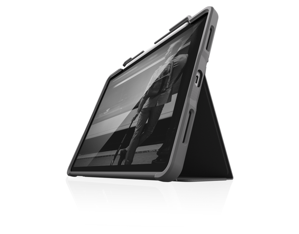 An iPad encased in the STM Dux Plus Case for iPad Air M2/M3/M4/4th/5th Gen by STM is shown propped in landscape mode, displaying a grayscale image of a person standing outdoors near a large modern structure.