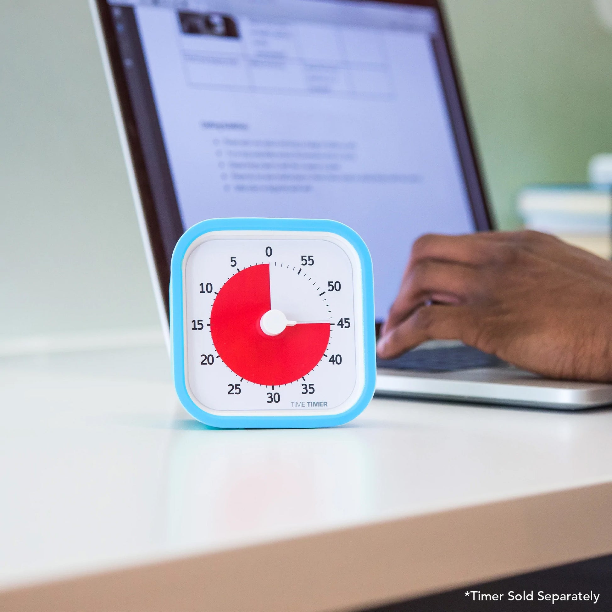 A person types on a laptop at a desk, with a Time Timer MOD Cover Silicone Case Accessory by Time Timer showing about 15 minutes left in the foreground. "Timer Sold Separately" appears in the corner.