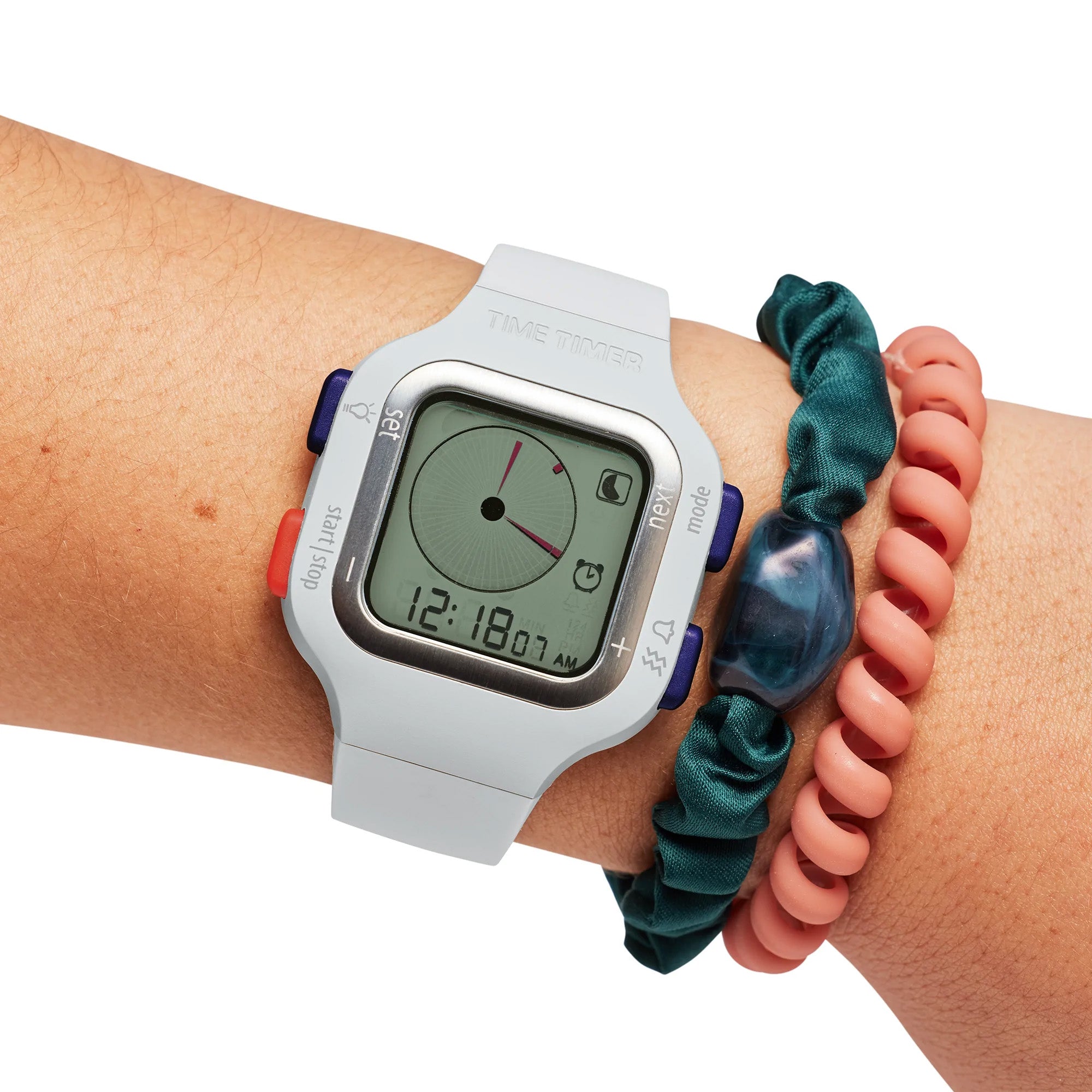 A wrist sports a Time Timer Watch (Small/Youth) by Time Timer, showing 12:18. The digital face is clear and easy to read, with a teal scrunchie and pink coil bracelet alongside it, making time tracking simple for kids.