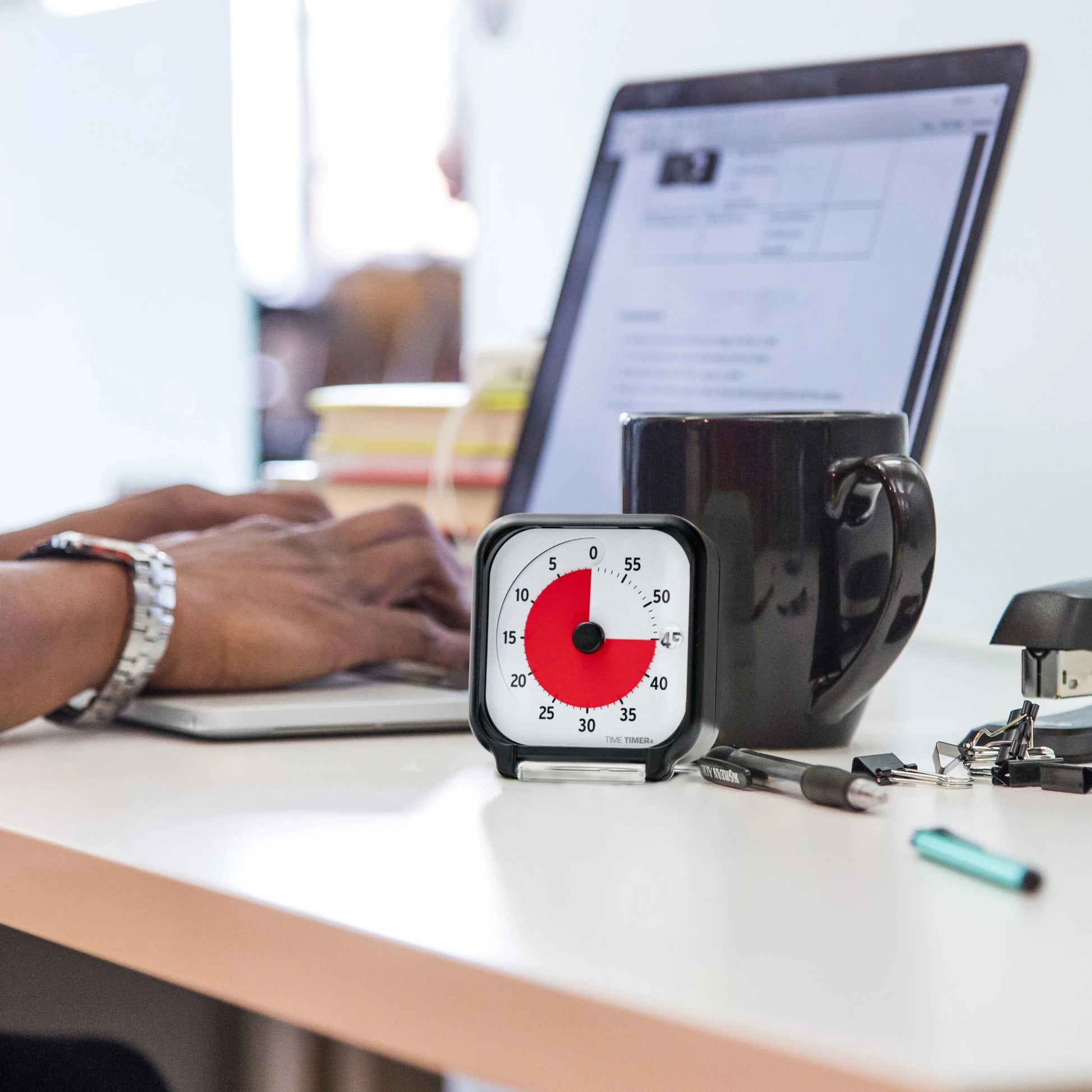 A person types at a desk with a black mug, pen, and keys beside the Time Timer Original (3 Inch) Pocket [Black] Red Disk by Time Timer, set for 25 minutes—highlighting workspace essentials for effective time management.