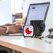 A time timer 3 inch with a person working on a laptop in the background and some stationery in the foreground.